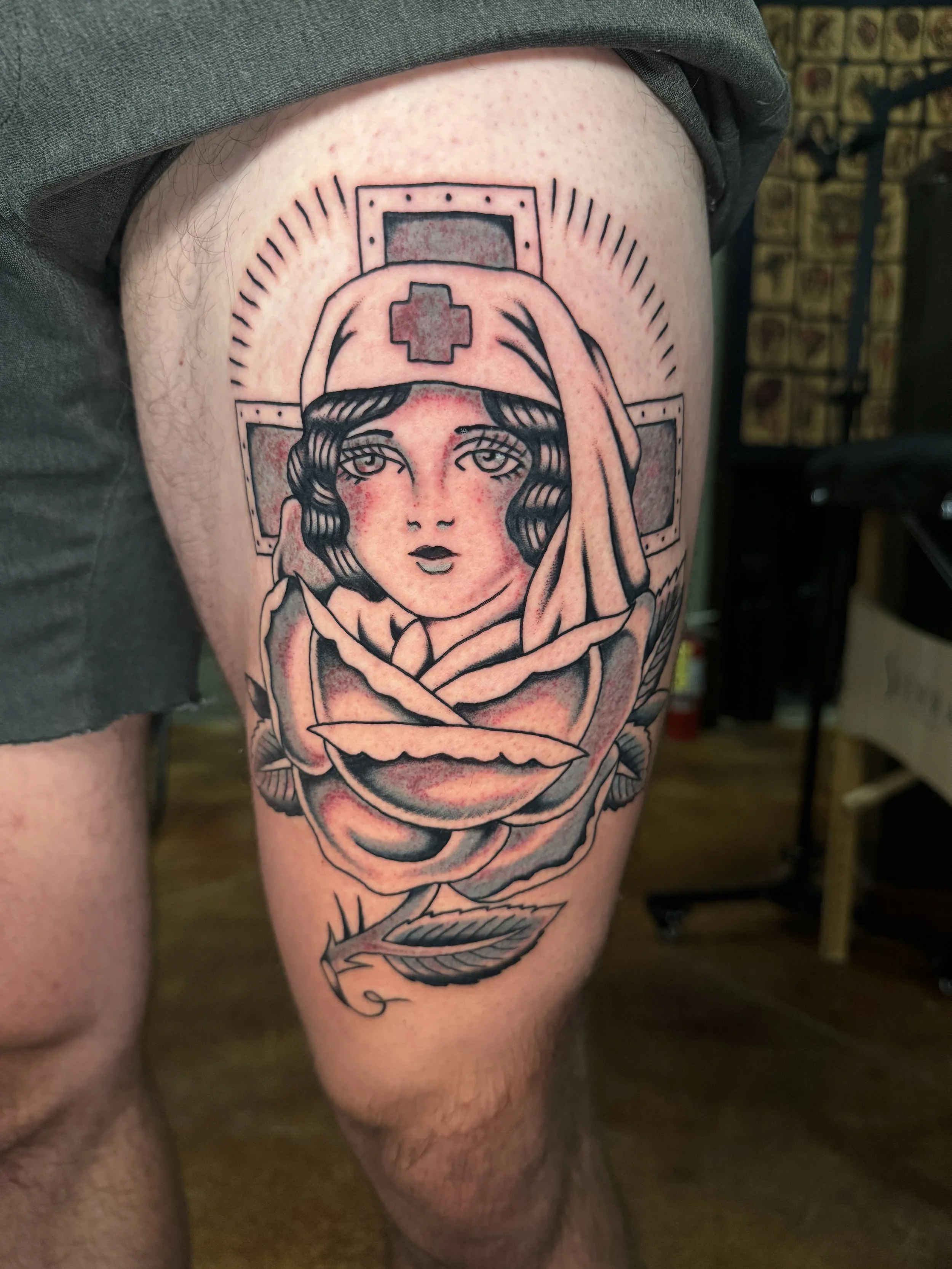 Tattoo of a nurse woman on a person's thigh. The nurse has a vintage style with short hair, a nurse's cap with a red cross, and is holding a rose in her hand.