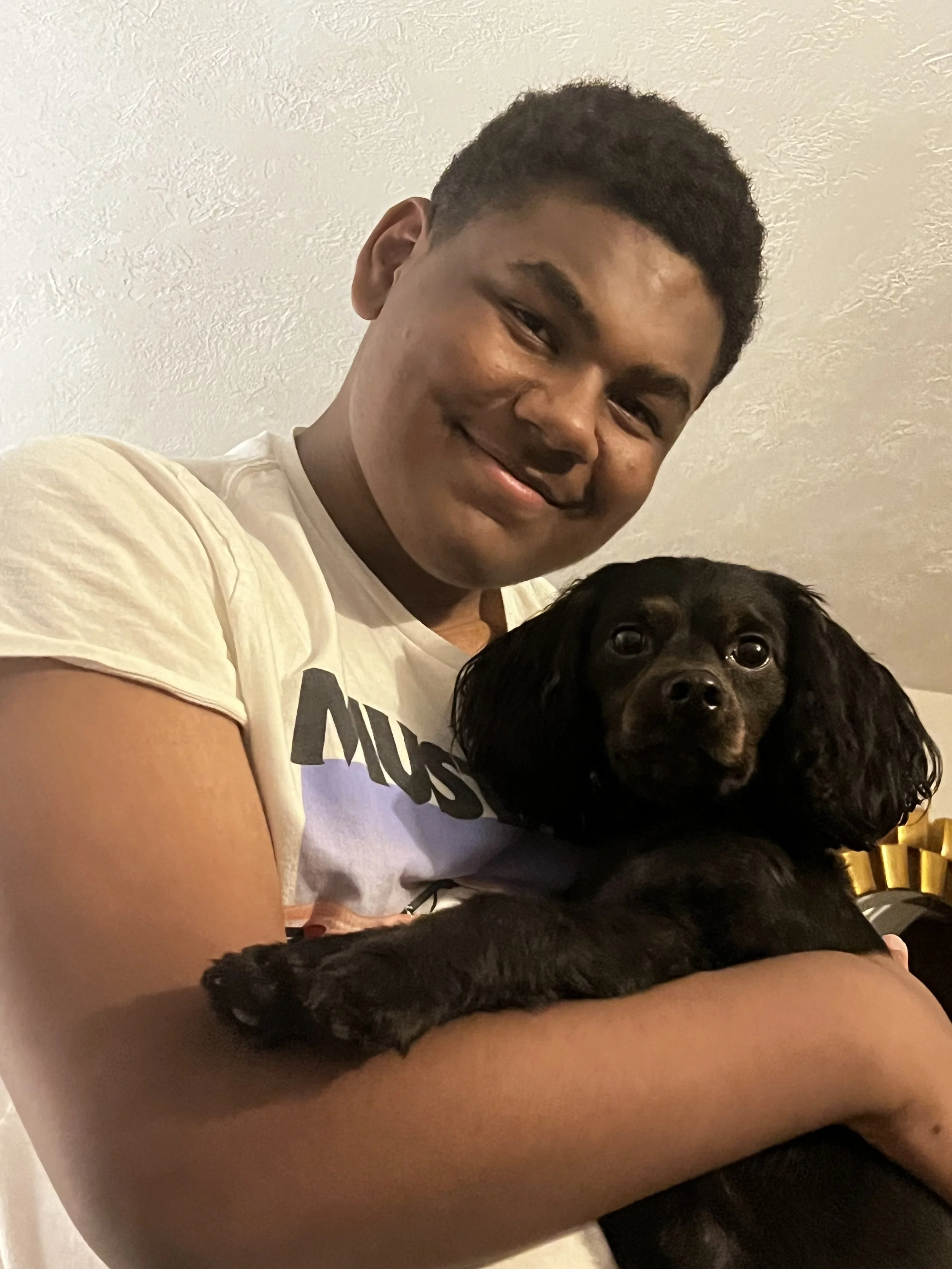 A young boy smiling while holding a black dog with long ears and shiny fur.