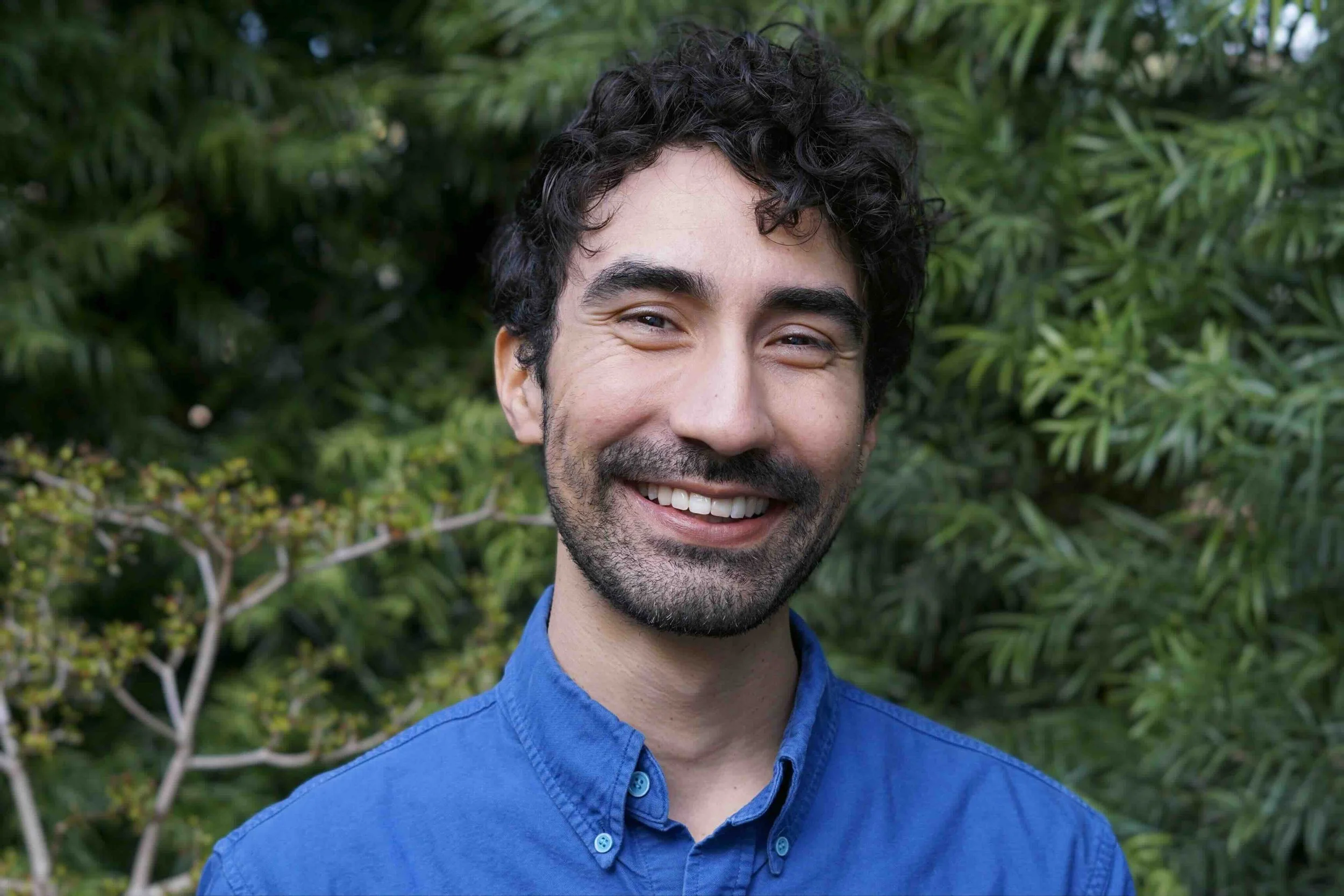 Michael Olivares PhD. Brown multiracial latino therapist in blue button down. Leaves in background.