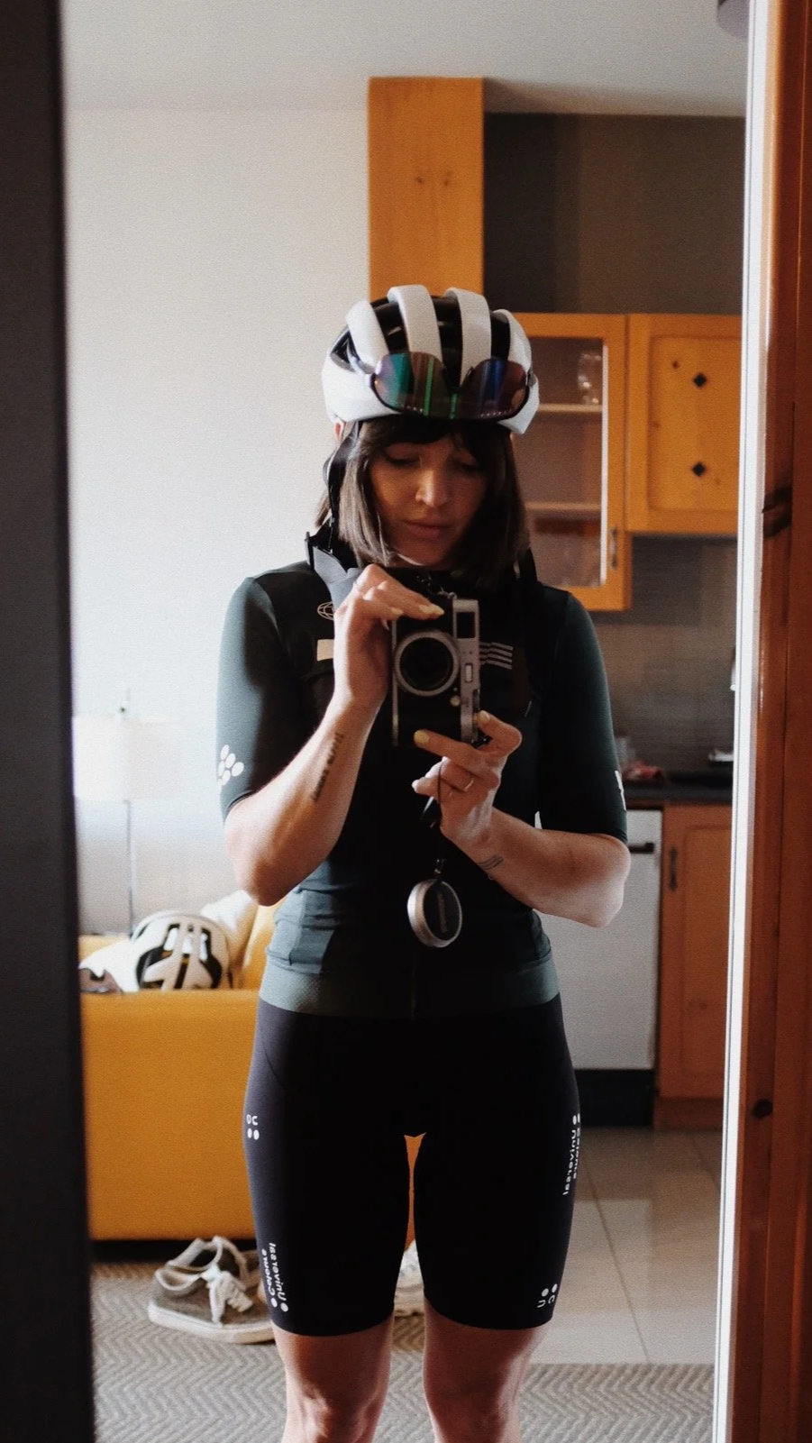 Femme en tenue de cyclisme prenant une photo dans un miroir, portant un casque de vélo avec lunettes, en intérieur d'appartement.