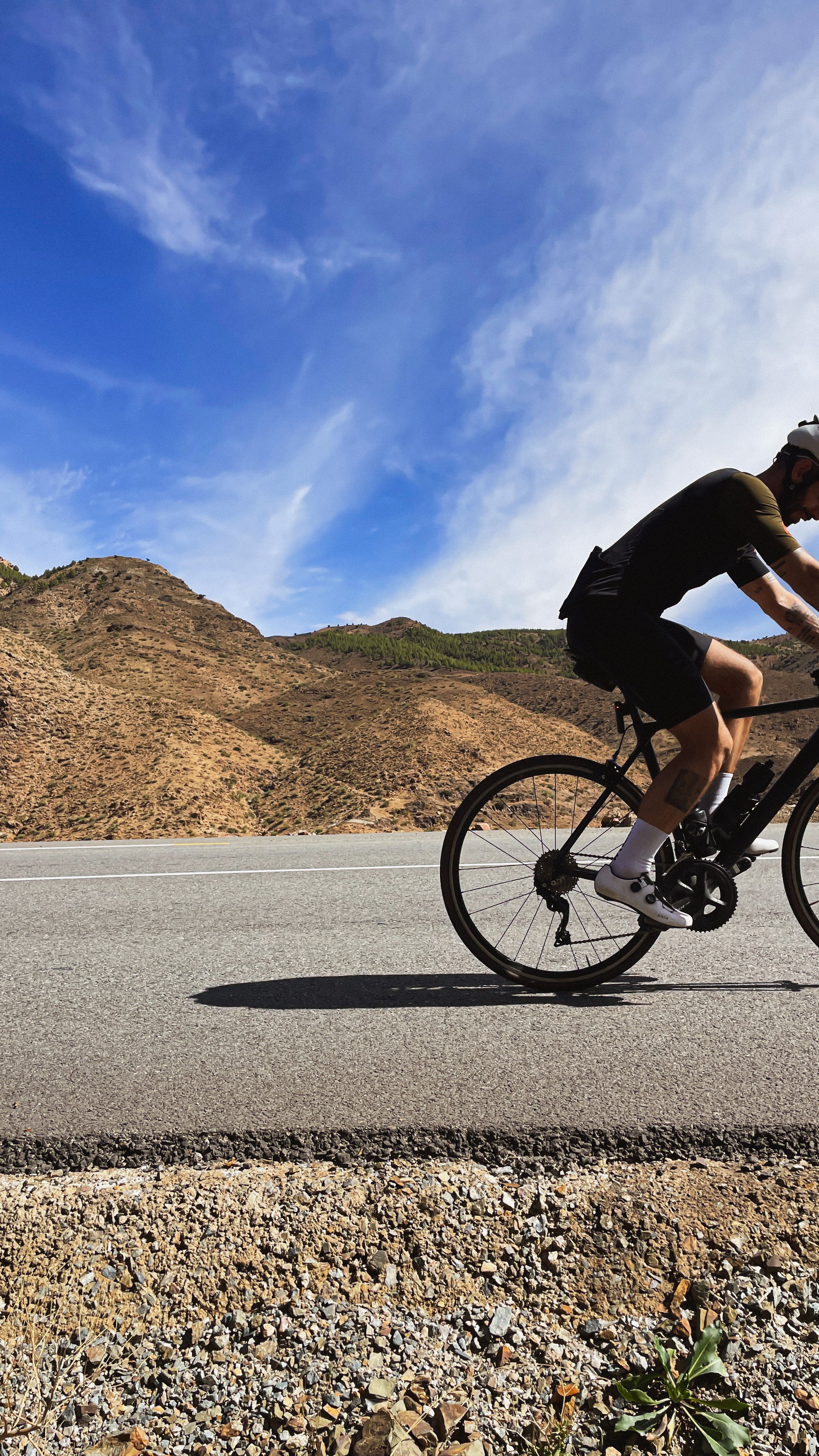 Un cycliste en mouvement sur une route montagneuse avec un ciel bleu et nuageux.