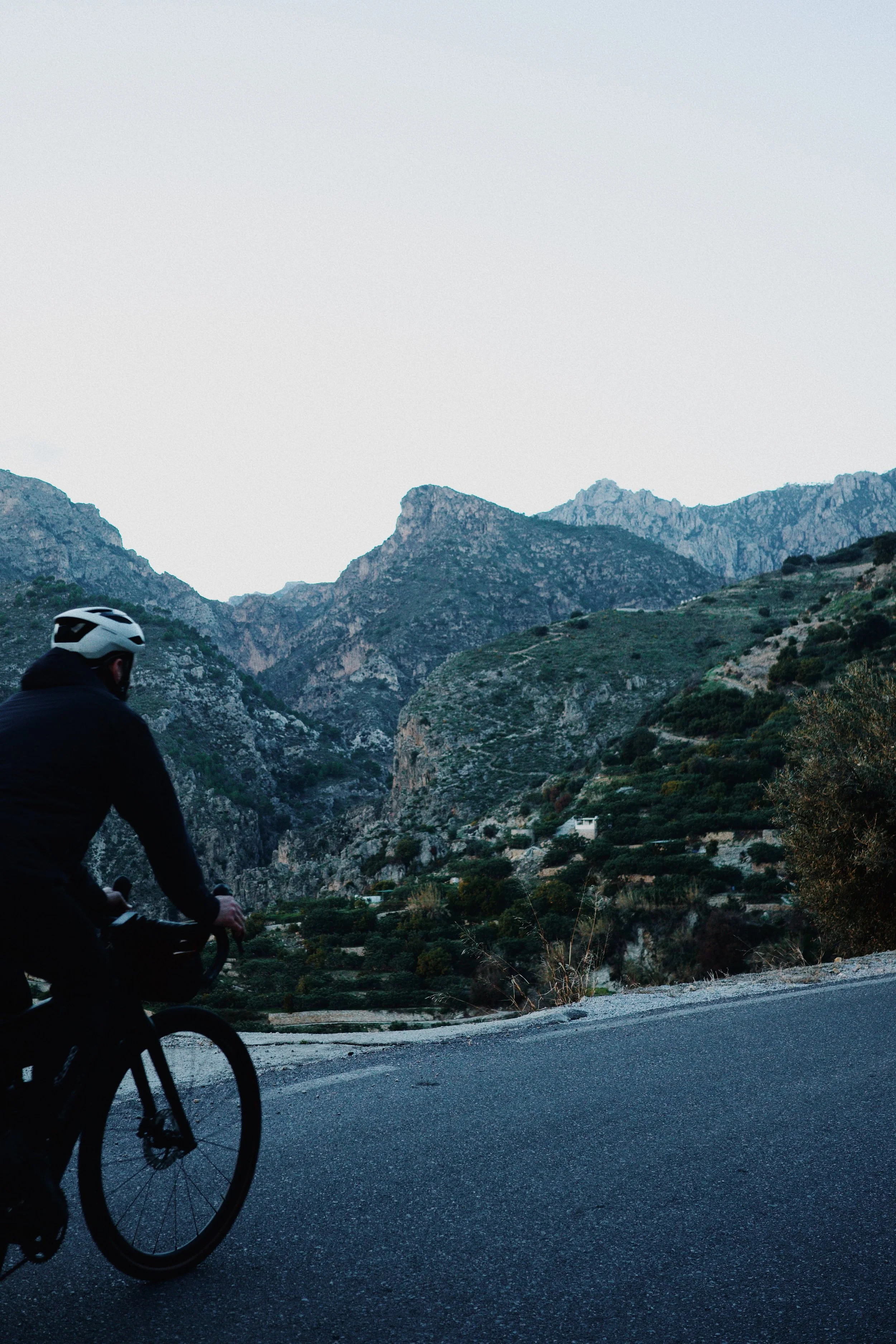Cycliste portant un casque noir roulant sur une route montagneuse entourée de montagnes rocheuses et de végétation