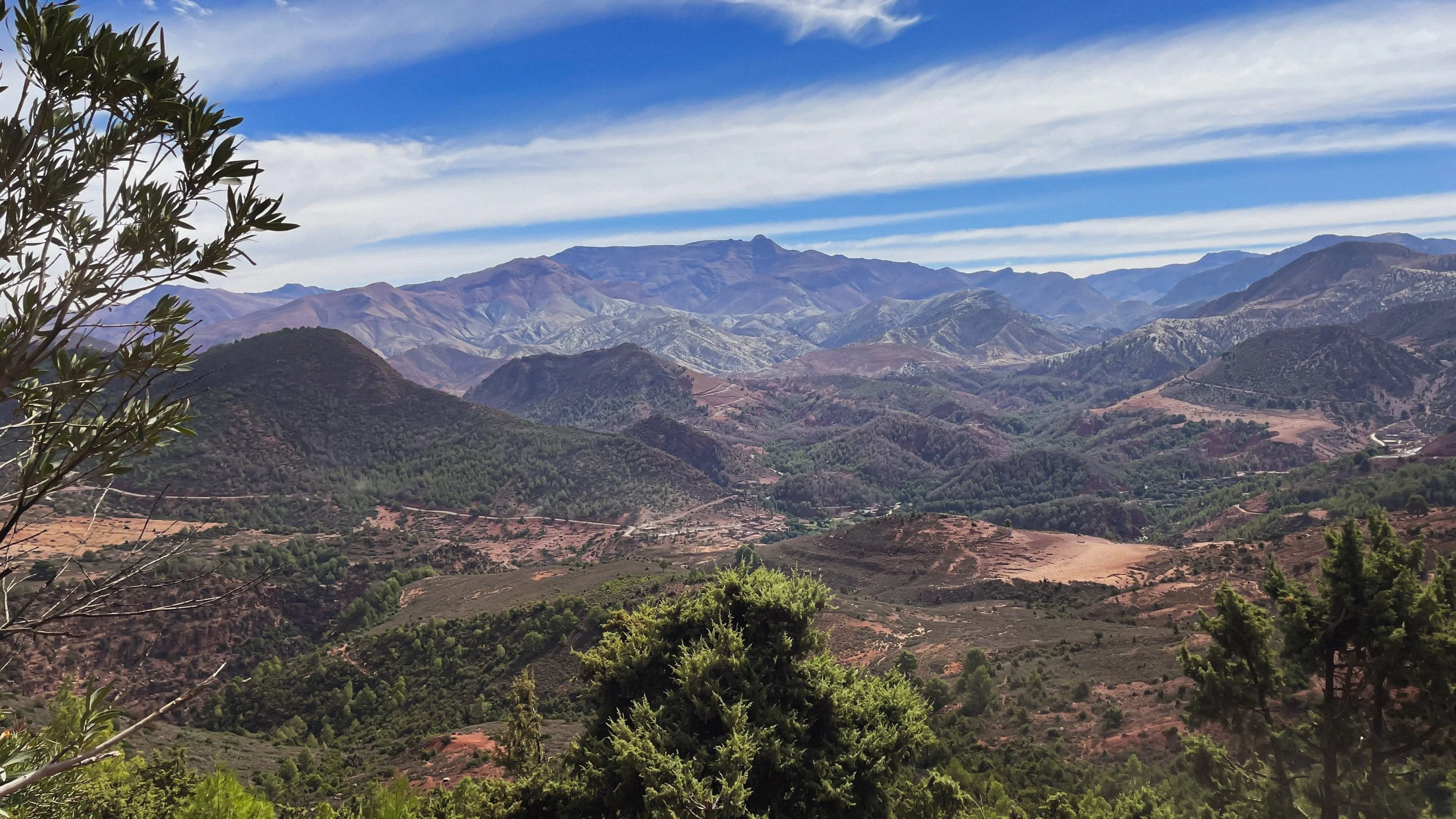 Paysage de montagnes avec ciel bleu et nuages, végétation au premier plan.