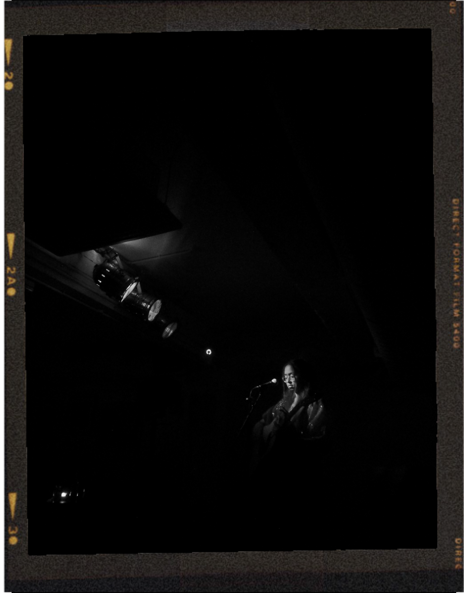 A woman playing guitar and singing on a dark stage in a dimly lit venue.