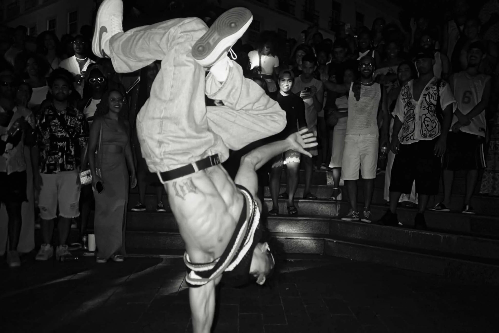 A person dressed in a panda costume performing a dance move in front of an audience on steps at night.