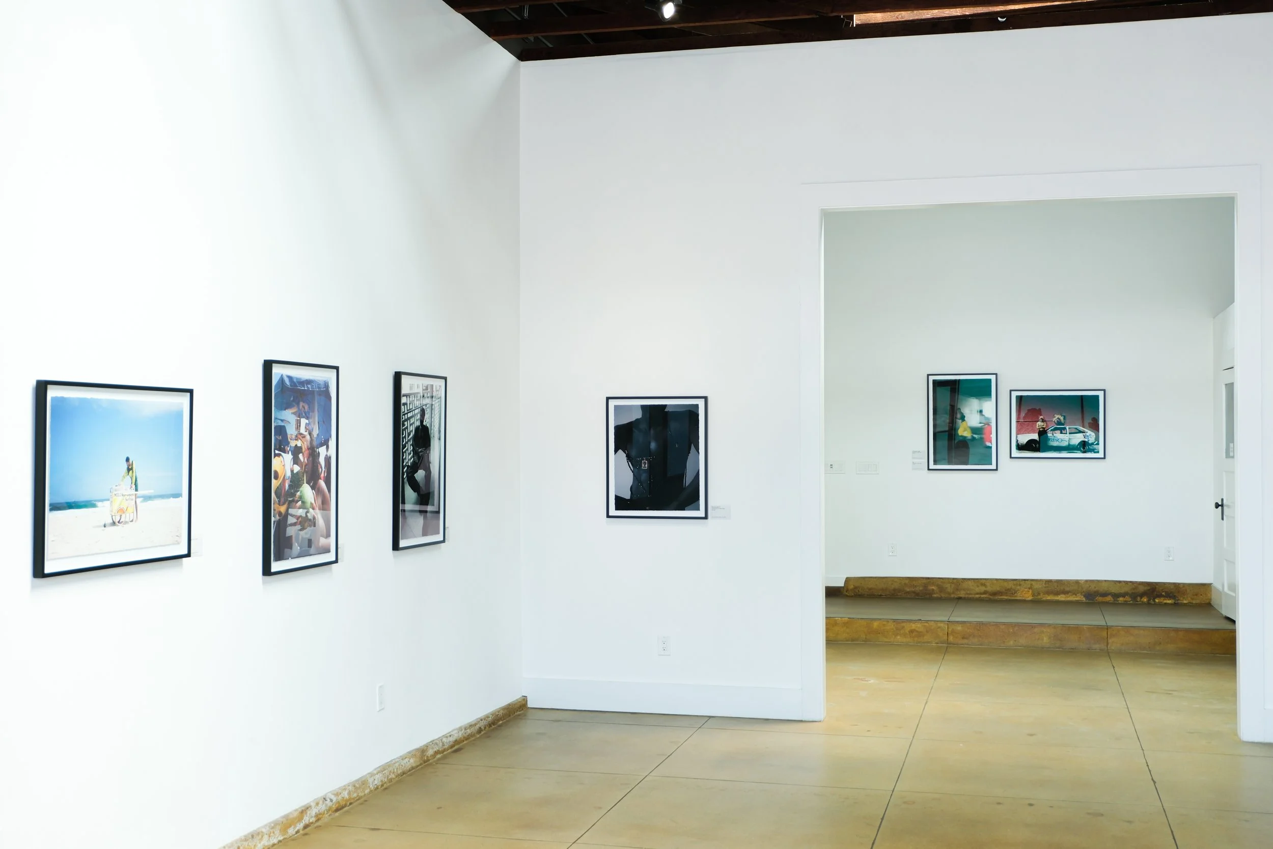 Gallery with framed photographs on white walls and wooden ceiling beams.