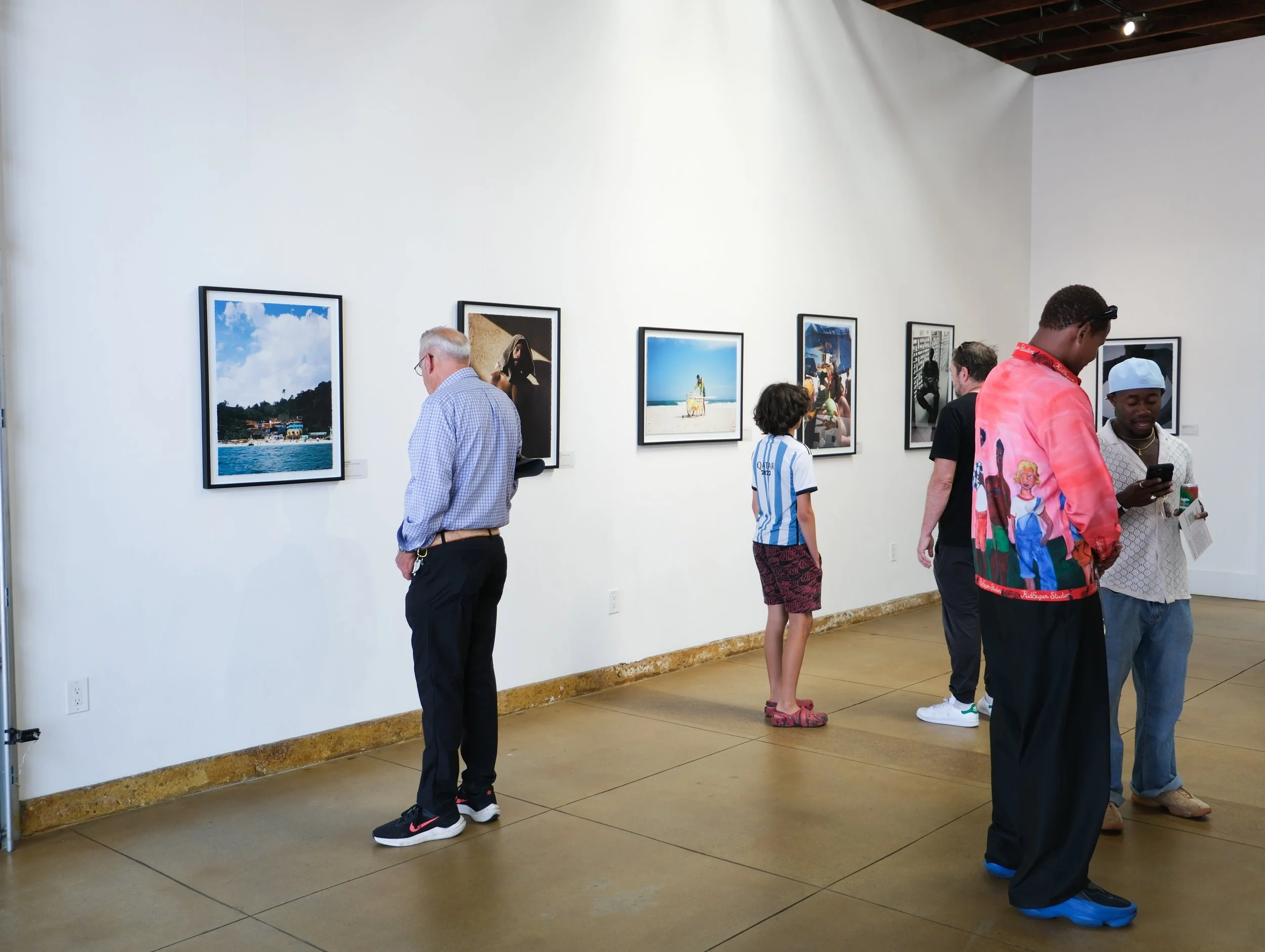 People viewing framed photographs on a gallery wall at an art exhibition.