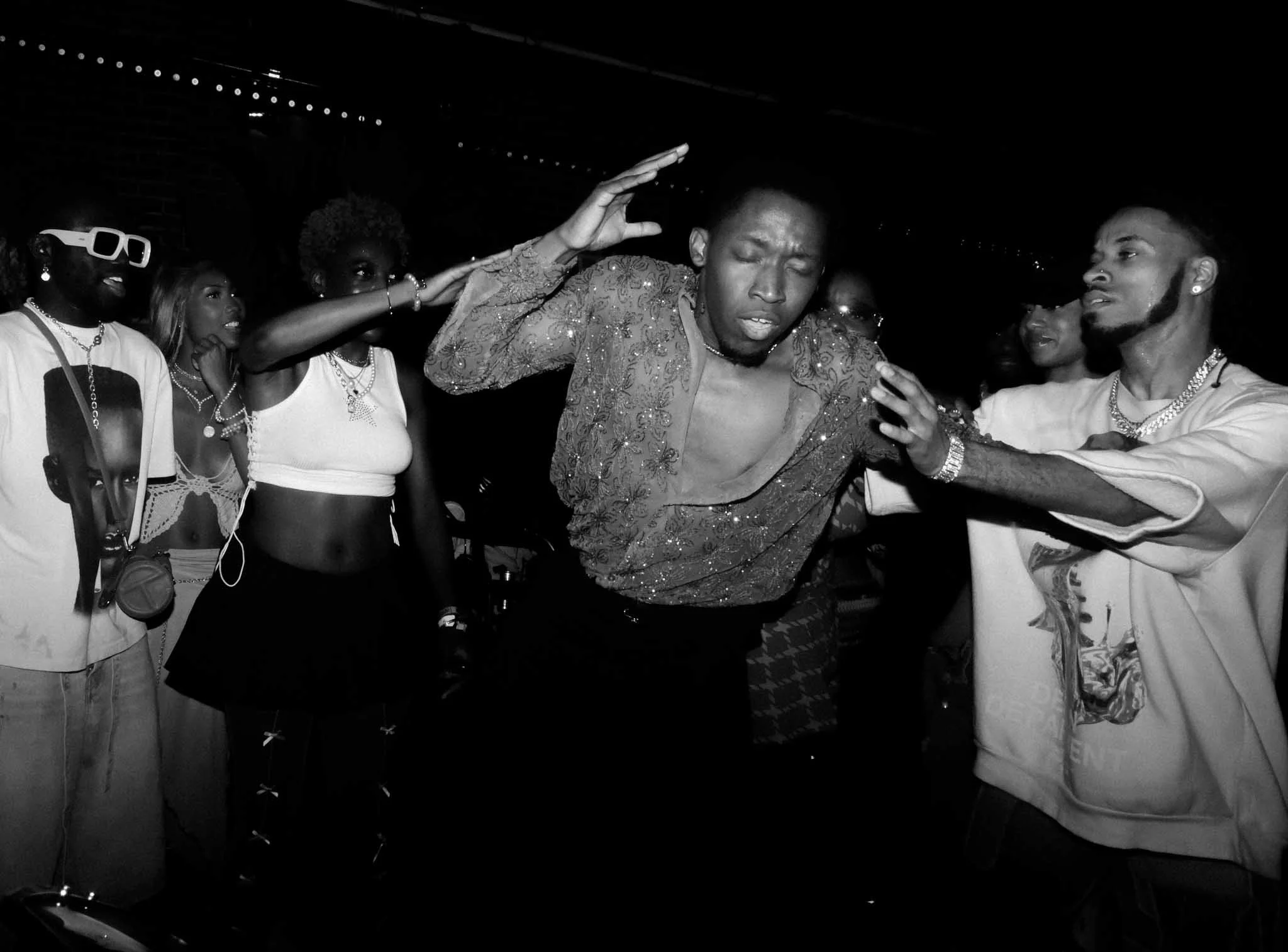 People dancing at a party, with some wearing jewelry and casual attire, with a dark background.