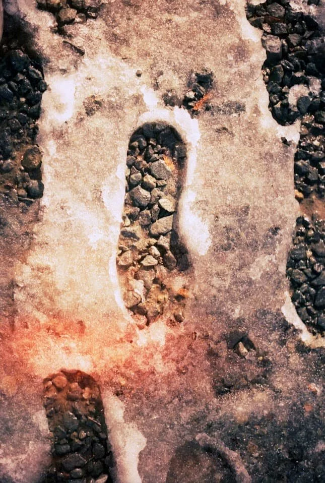 Footprint in dirt showing embedded small rocks and dirt with some sunlight reflection.