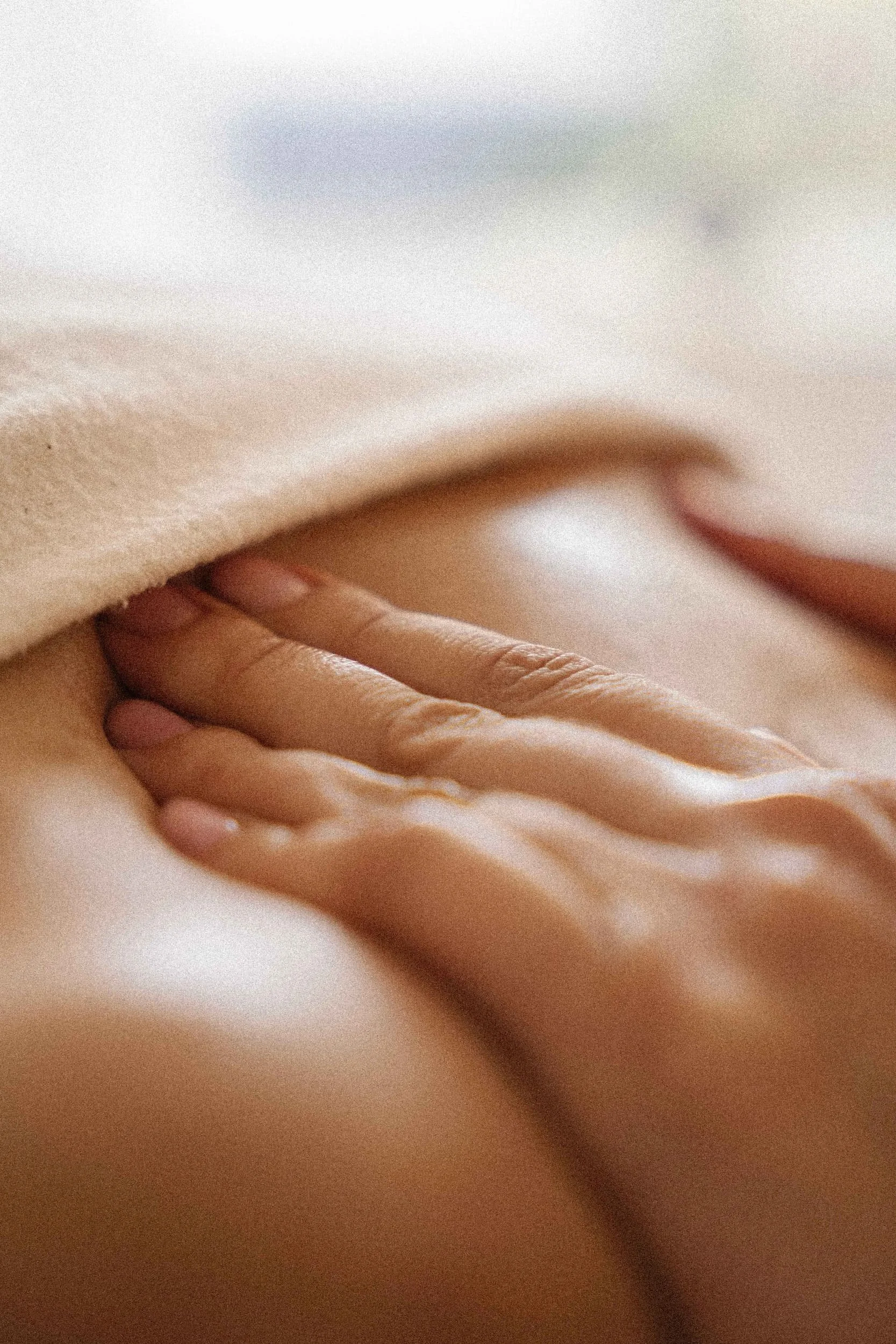 Close-up of a person's hand gently touching a person's shoulder, with skin visible and soft lighting.