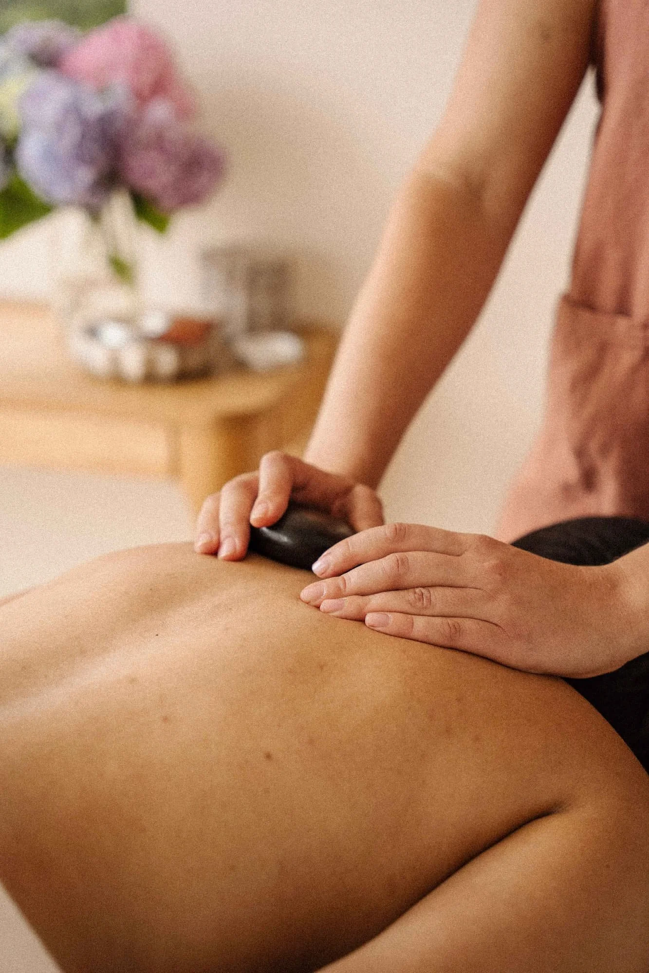Person receiving a massage on their back with massage stones in a relaxing indoor setting.