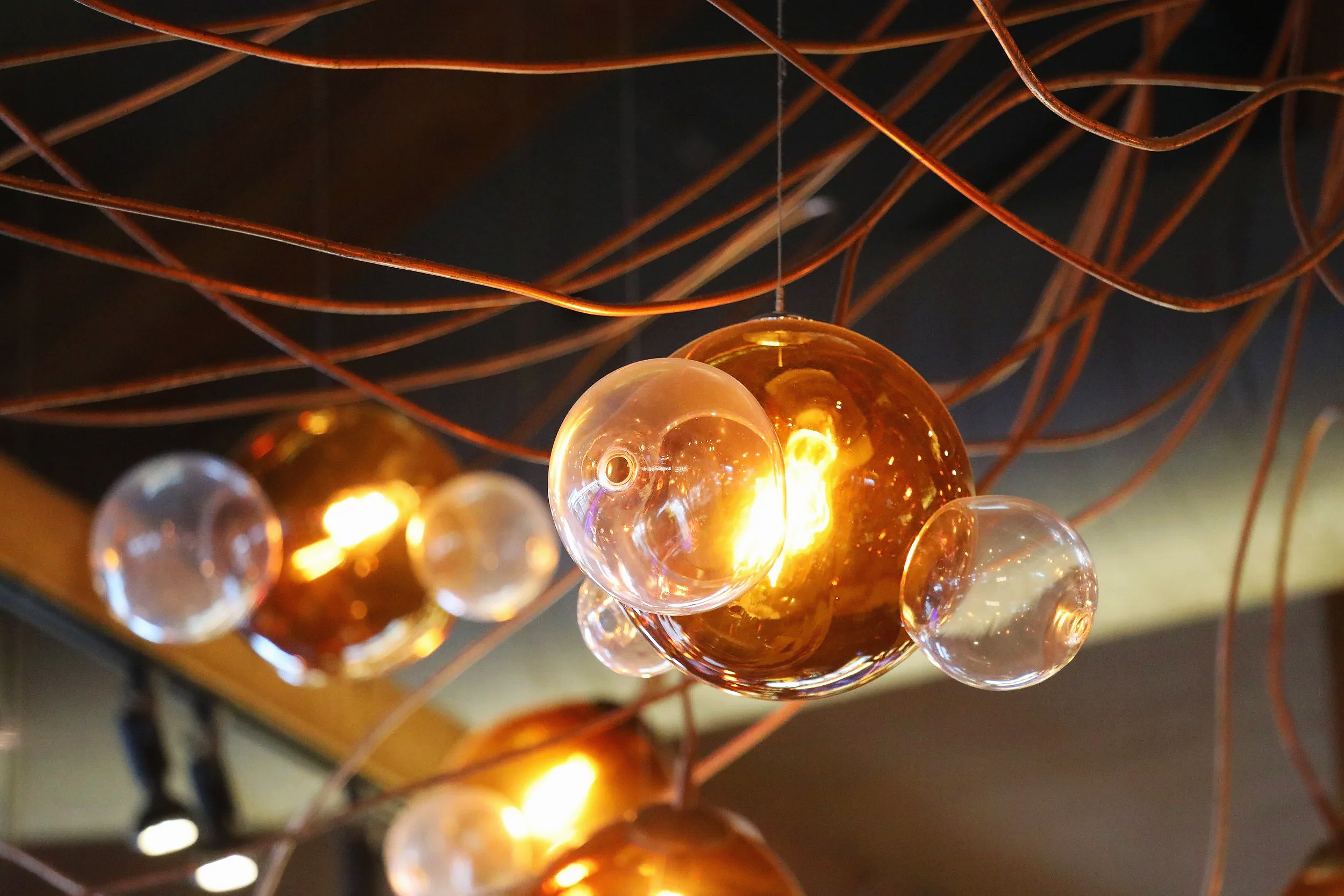 Close-up of decorative hanging glass orbs with warm lighting, suspended by a web of copper-colored wires.