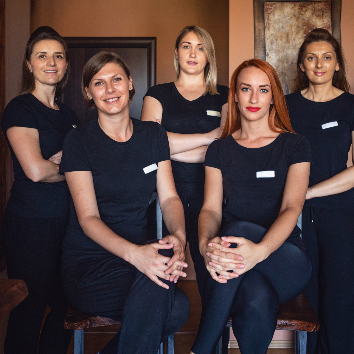 Group of five women wearing black shirts with name tags, posing together in an indoor setting.