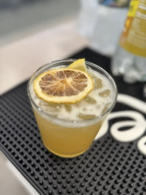 A glass of lemonade with lemon slices, placed on a black bar mat.