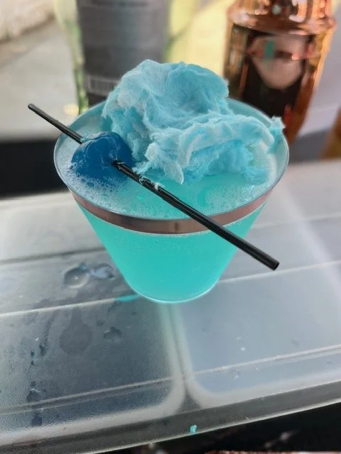 A blue cotton candy served in a martini glass with a black straw and a small black decorative stick.