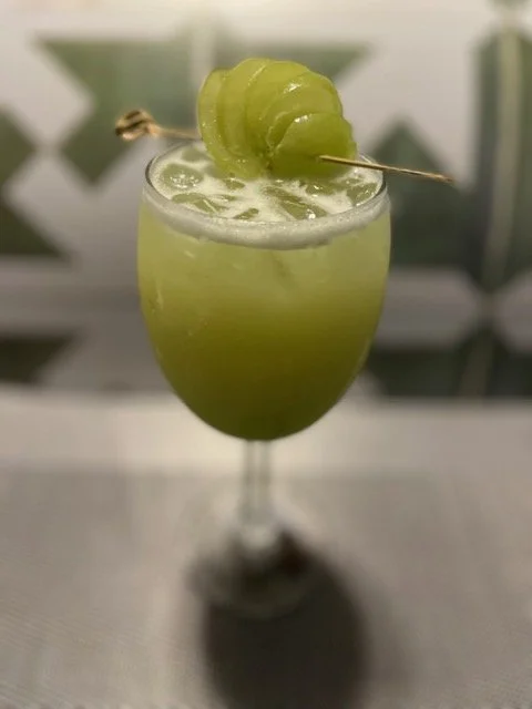 Green cocktail garnished with a lime twist on a skewer