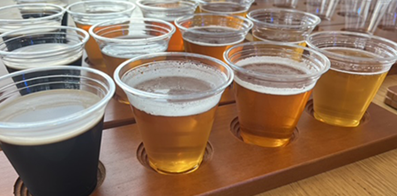 Various types of beer in plastic cups on a wooden tasting tray.