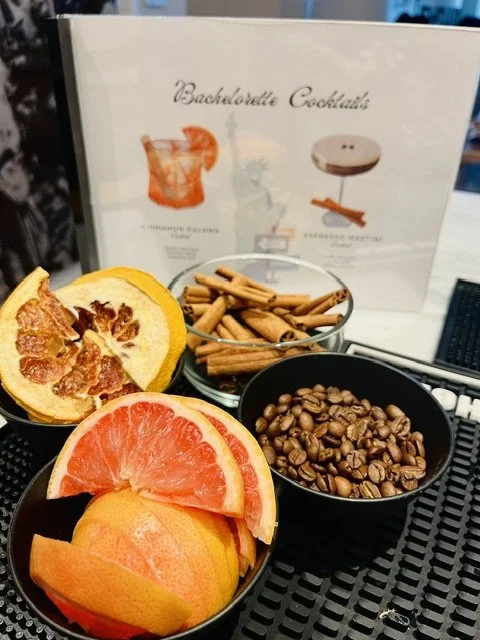 Bowls of sliced grapefruit and orange, a bowl of coffee beans, and a bowl of cinnamon sticks on a black table.