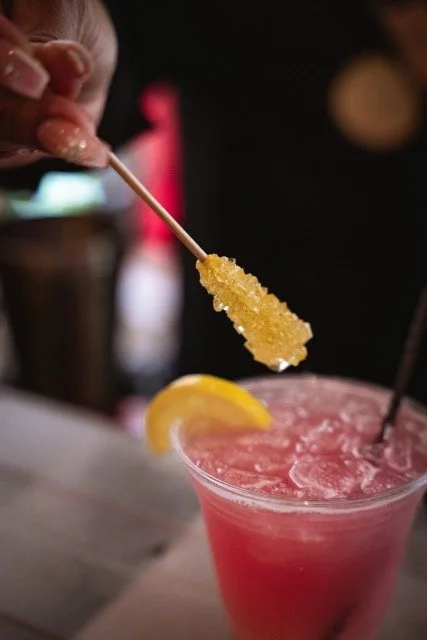 A pink frozen cocktail garnished with a lemon wedge, with a sugar-coated popsicle being dipped into it.
