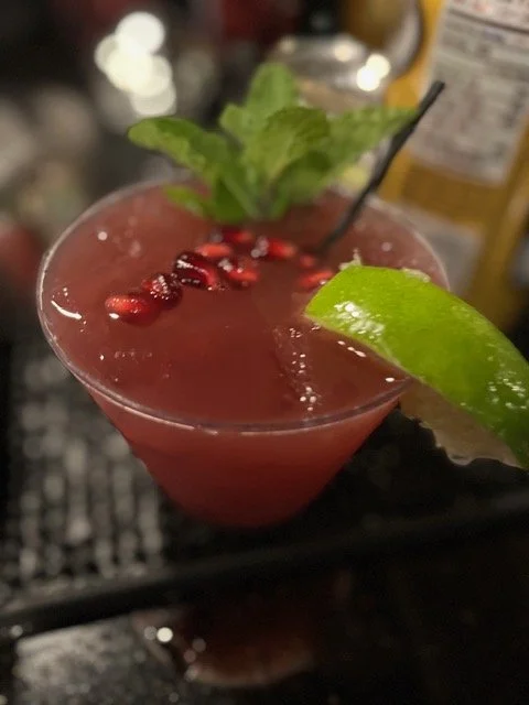 A cocktail garnished with pomegranate seeds, a lime wedge, and a sprig of mint.