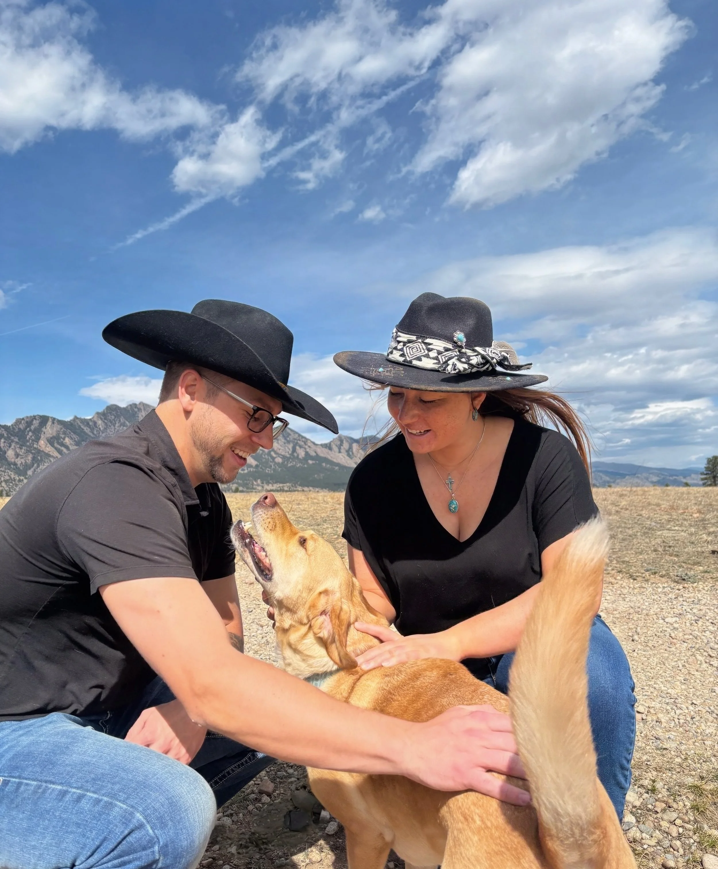 Chiropractors Dr. Ian, DC and Dr. Emma, DC and IVCA certified animal chiropractor look at their dog, Buddy, while petting him with mountains in the background near Westminster, CO