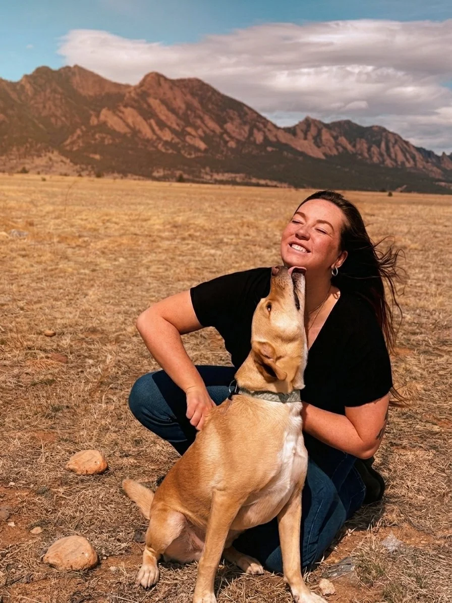 Dr. Emma, IVCA certified animal chiropractor smiles while adjusting a dog while the dog licks her chin in Westminster, CO