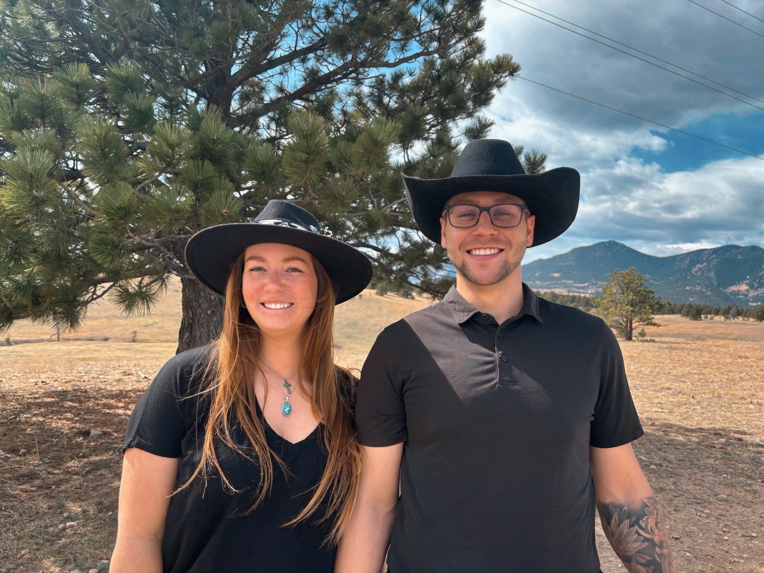 Dr. Emma, DC, IVCA and Dr. Ian, DC smile while standing in front of a tree with mountains in the background near Westminster, CO