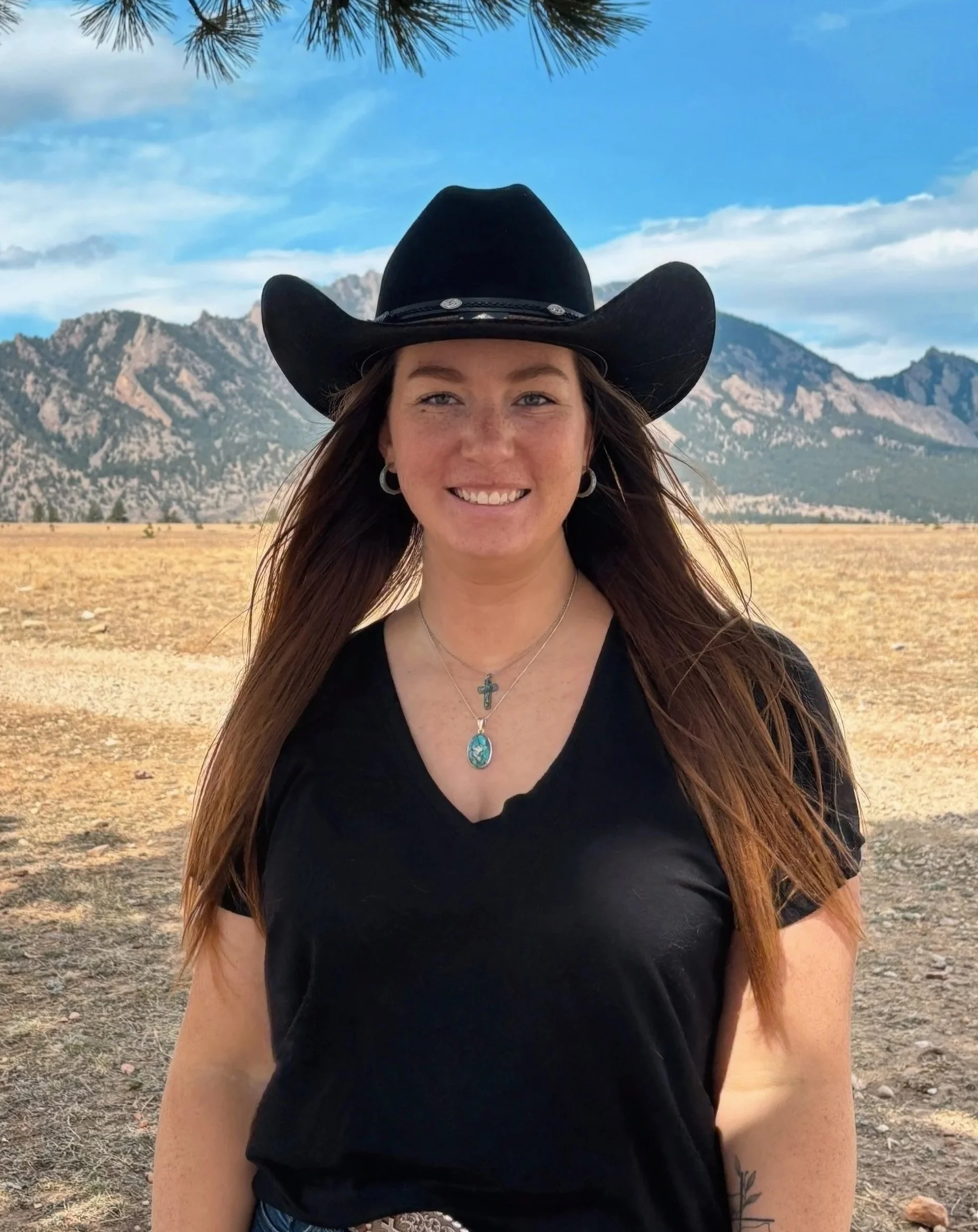 Dr. Emma, D.C. and Certified Animal Chiropractor, smiles in a cowboy hat while standing in front of the Flatiron Mountains near Westminster, CO