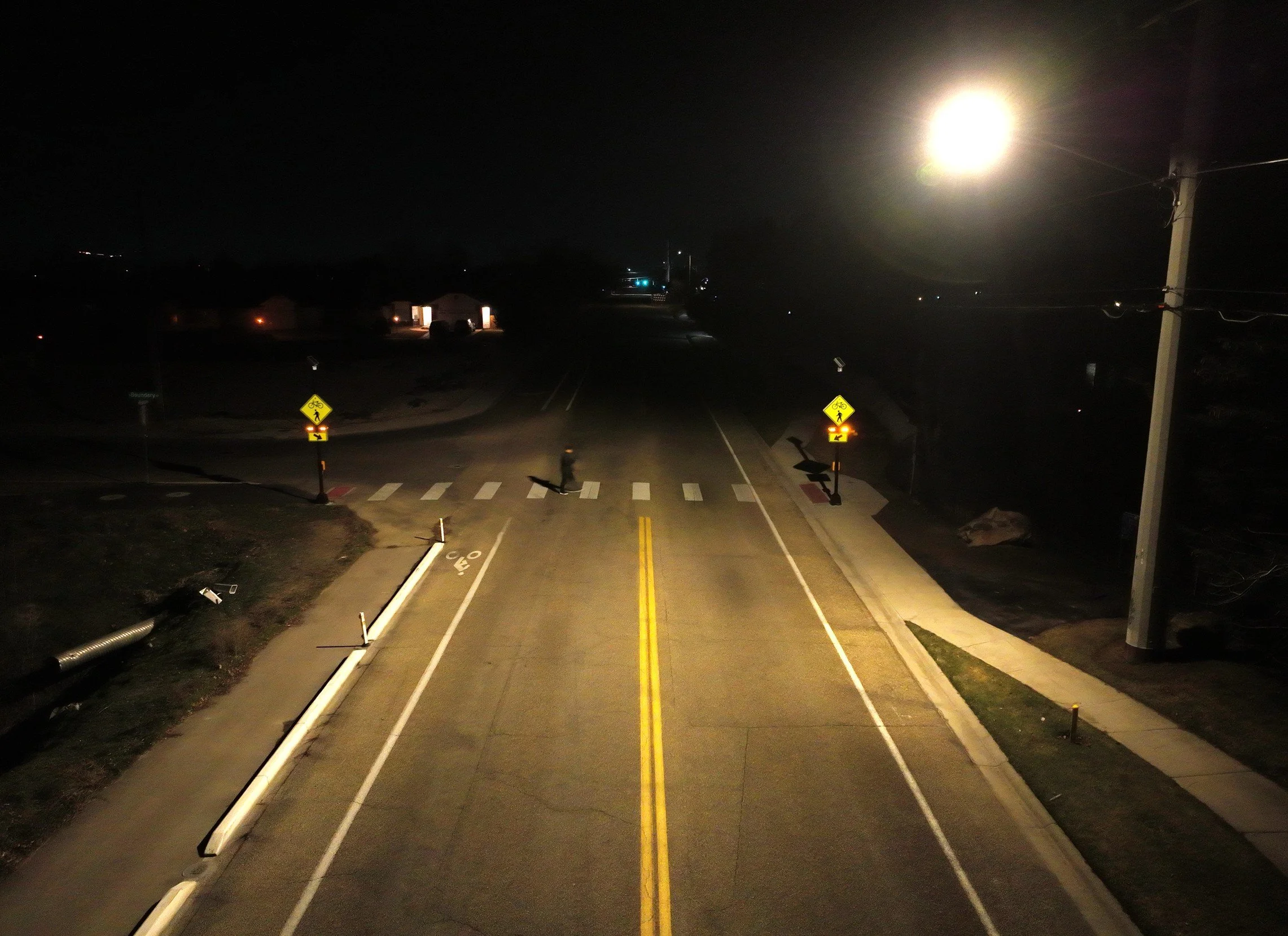 Nighttime view of a street intersection with traffic signs, streetlights, and utility poles illuminated by a bright full moon overhead.