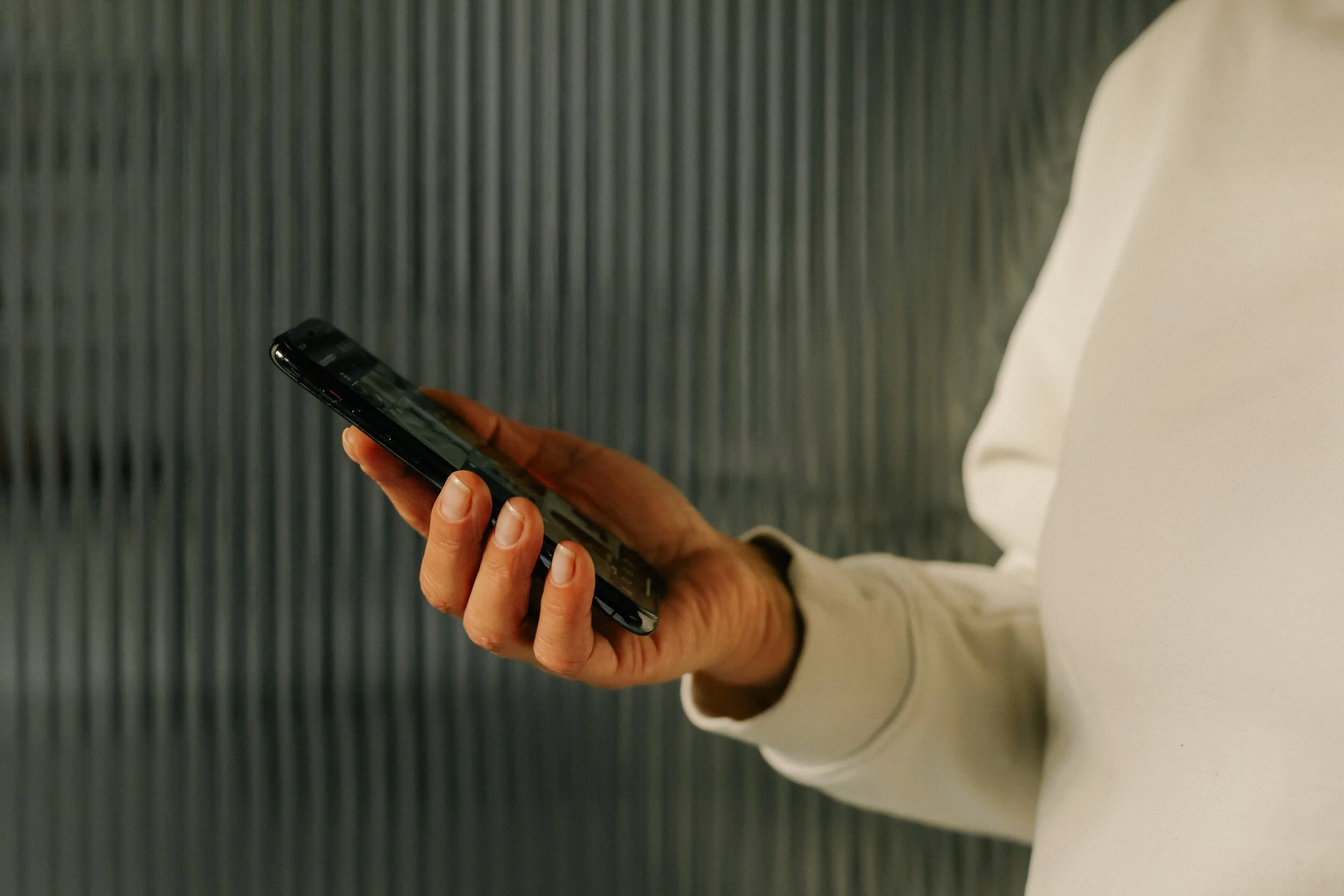 A person wearing a white long sleeve shirt holding a smartphone in their hands, standing on a gray carpeted floor.