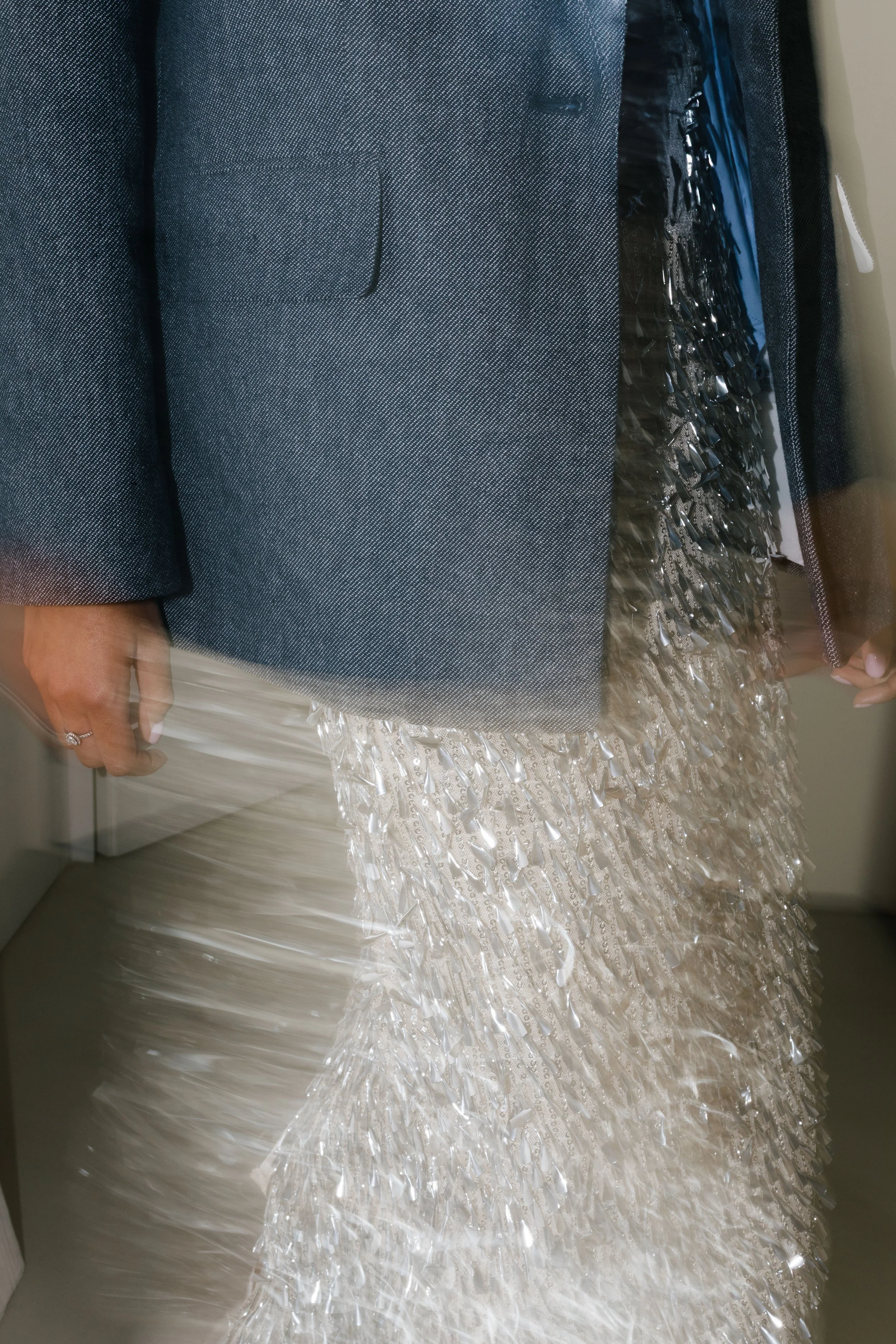 Close-up of a person in a gray suit on a wedding dress. The wedding dress has a textured, shiny, beaded skirt.