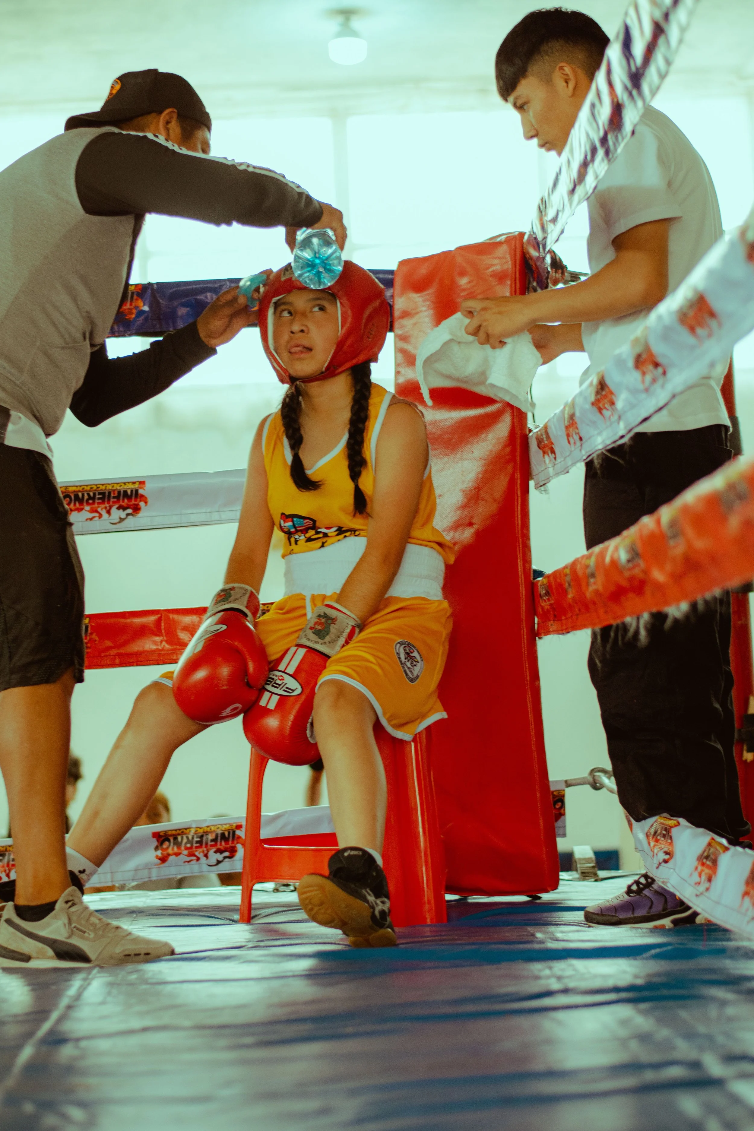 Young female boxer taking a water break and cooling down in the corner of a boxing ring between rounds.