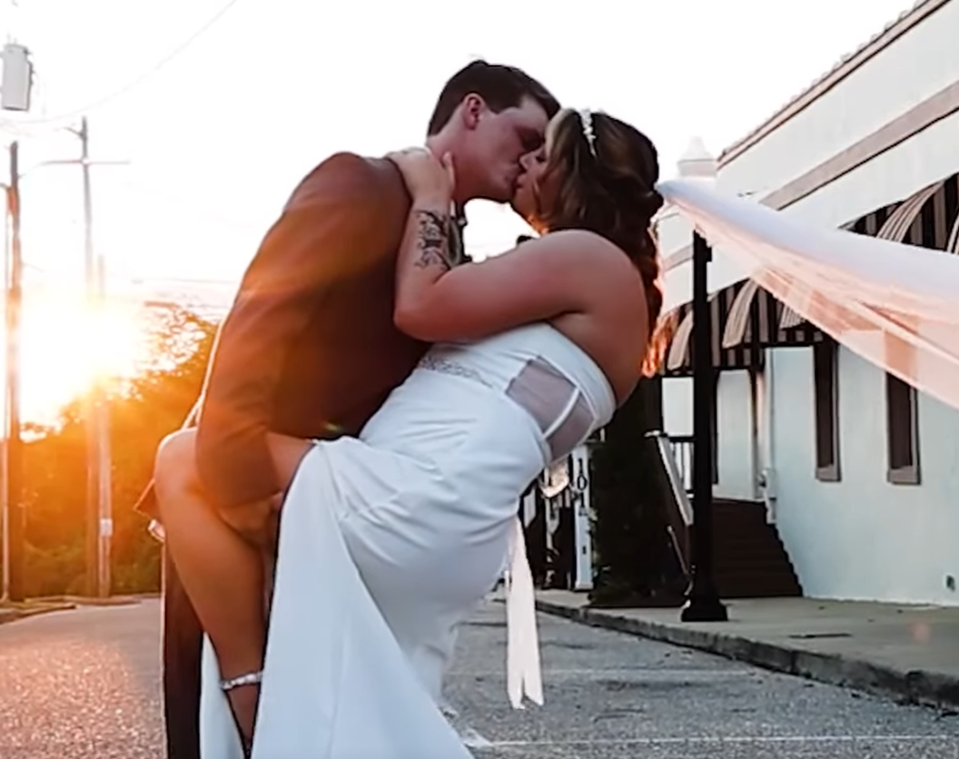 A couple sharing a romantic kiss outdoors during sunset, with one person lifting the other.