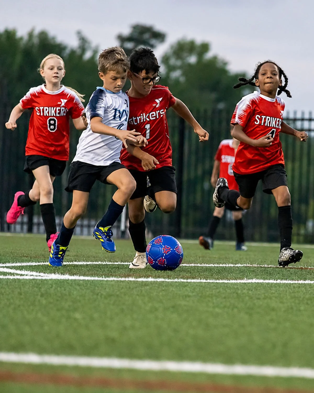 Kids from the YMCA playing soccer, competing for the ball on a field, wearing red and white jerseys with numbers.