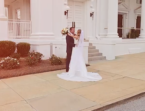 Bride and groom sharing a kiss outside a white building with stairs and columns.
