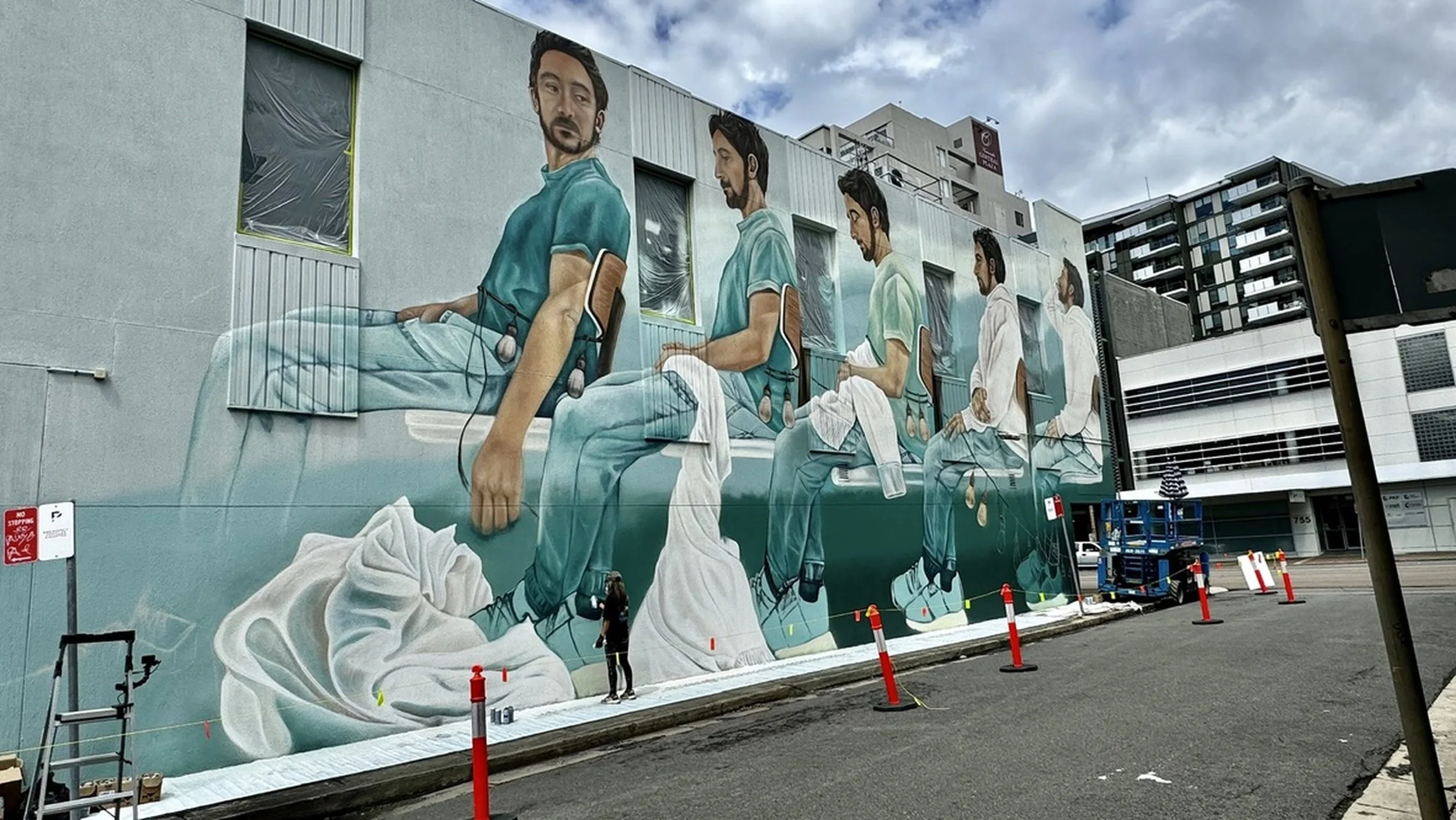Large mural of patients in a hospital emergency room, painted on a building wall, depicting various stages of medical care and items like a skull and medical equipment.