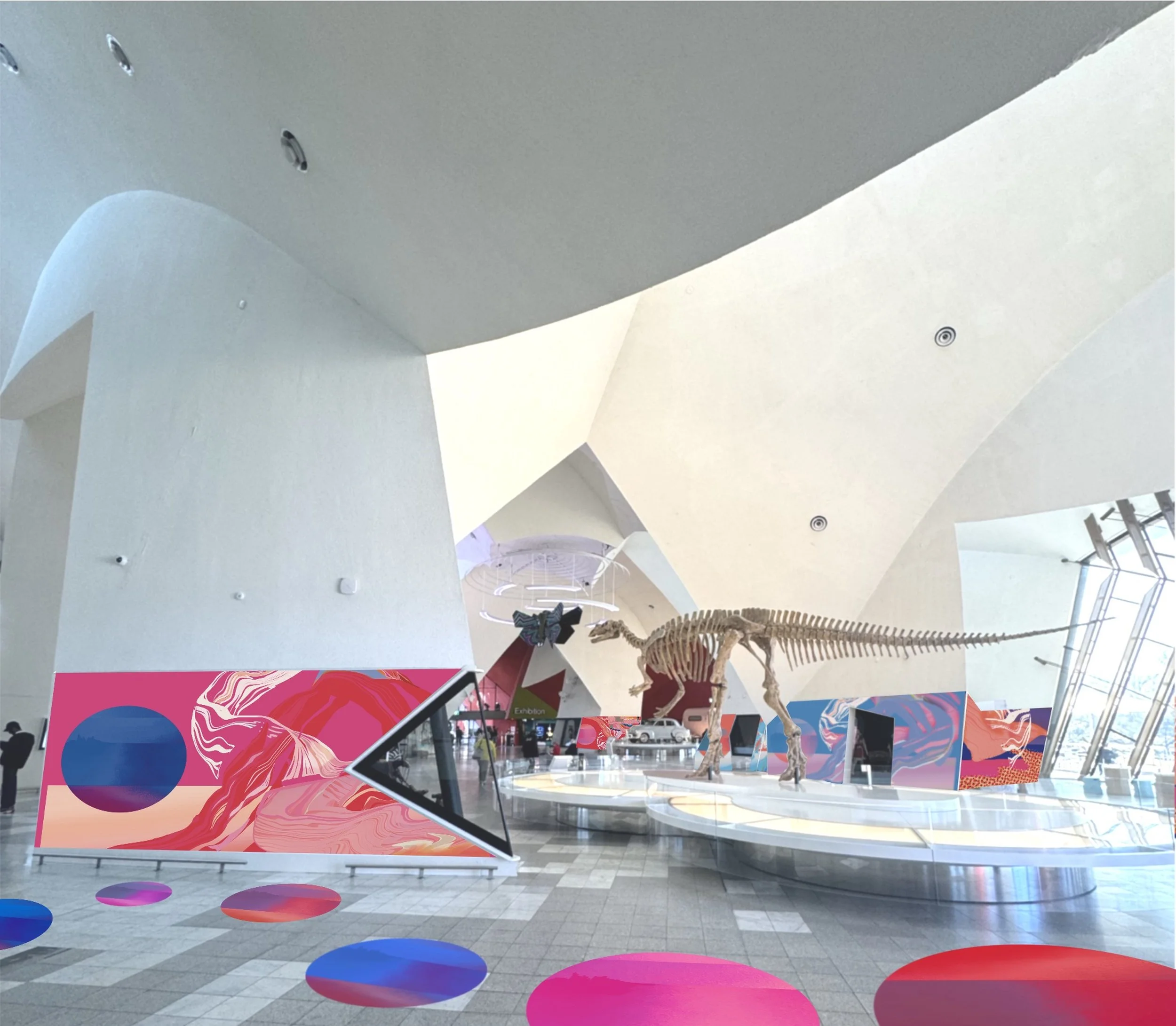 Interior of a modern building with white walls, a white ceiling, and colorful abstract art displays. There are dinosaur skeleton models and digital screens, with a floor decorated with colorful circular patterns.