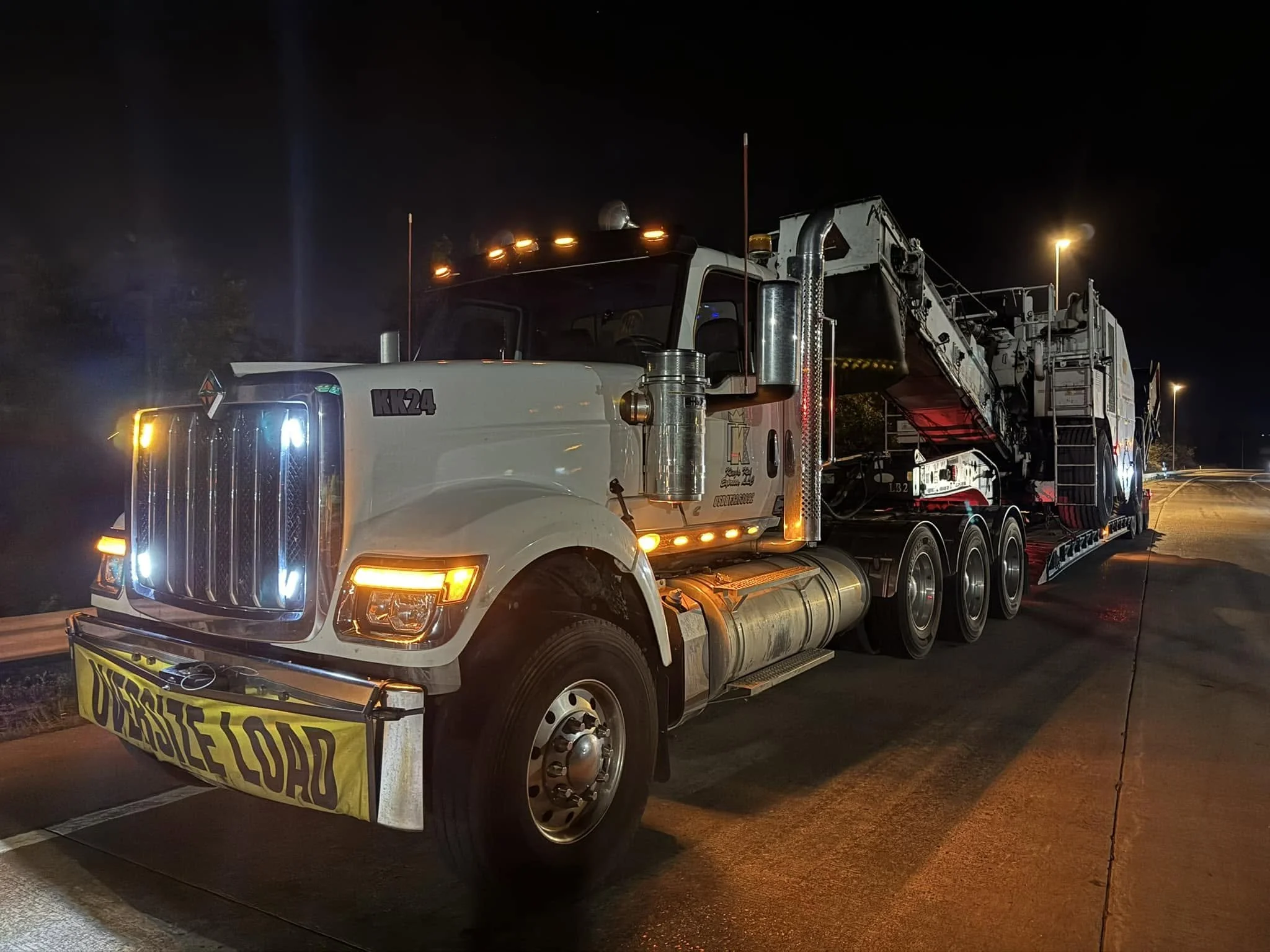 White King’s Kid Express truck with an oversize-load banner transporting heavy equipment at night.