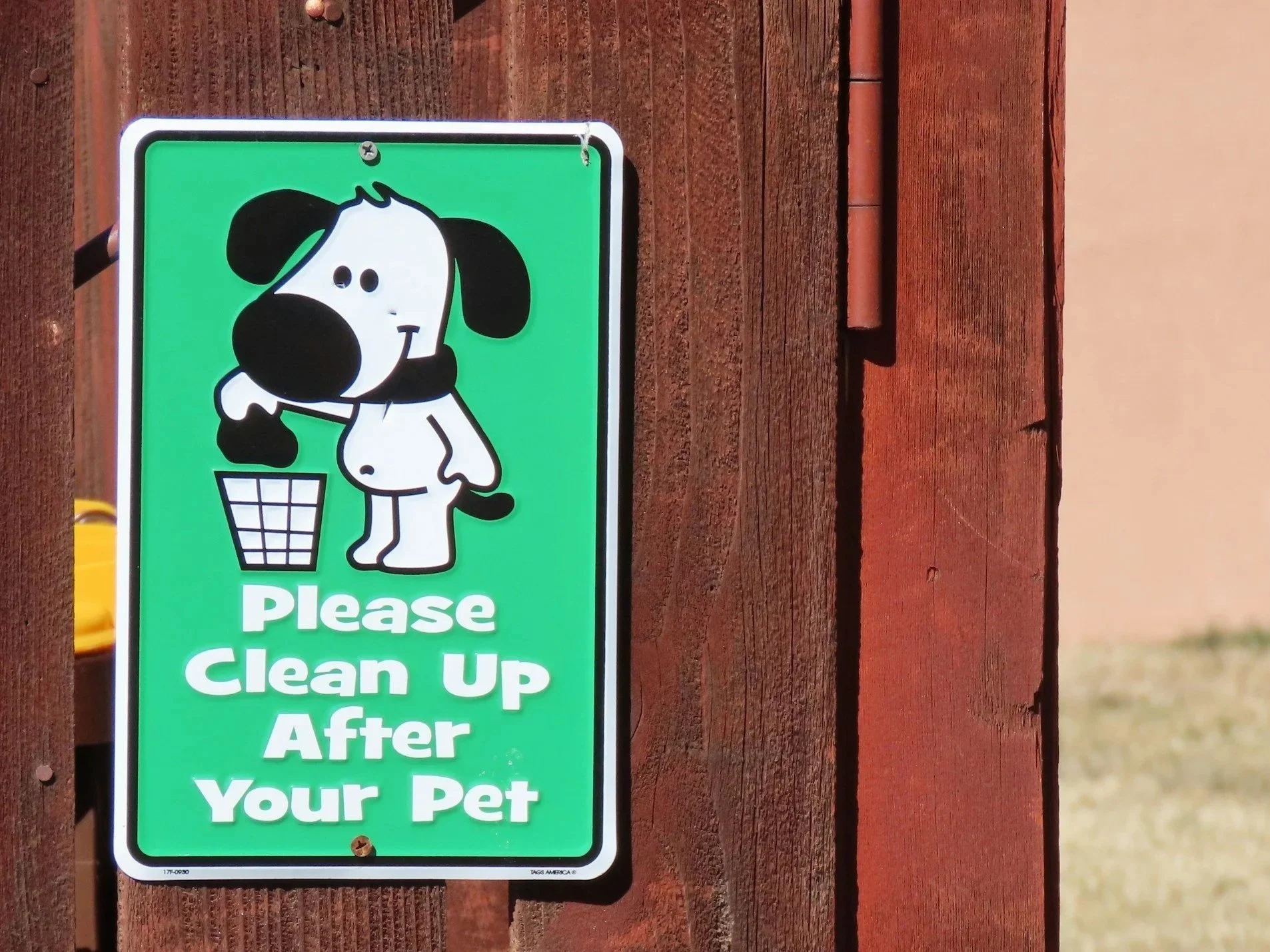 Green sign with a cartoon dog standing next to a trash can, asking to clean up after your pet.Dog Poop clean up.
