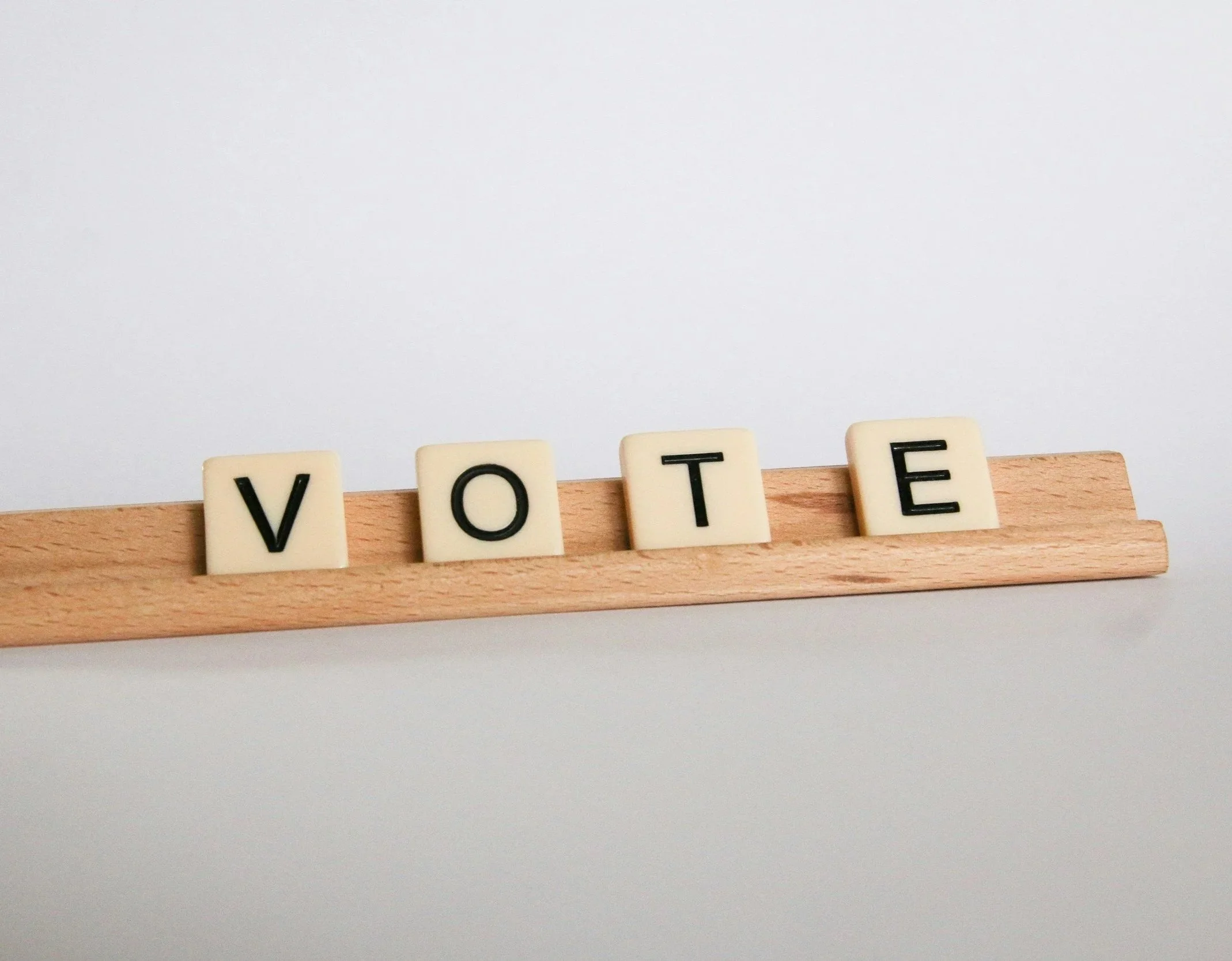 Scrabble tiles spelling the word 'VOTE' placed on a wooden surface against a plain white background.