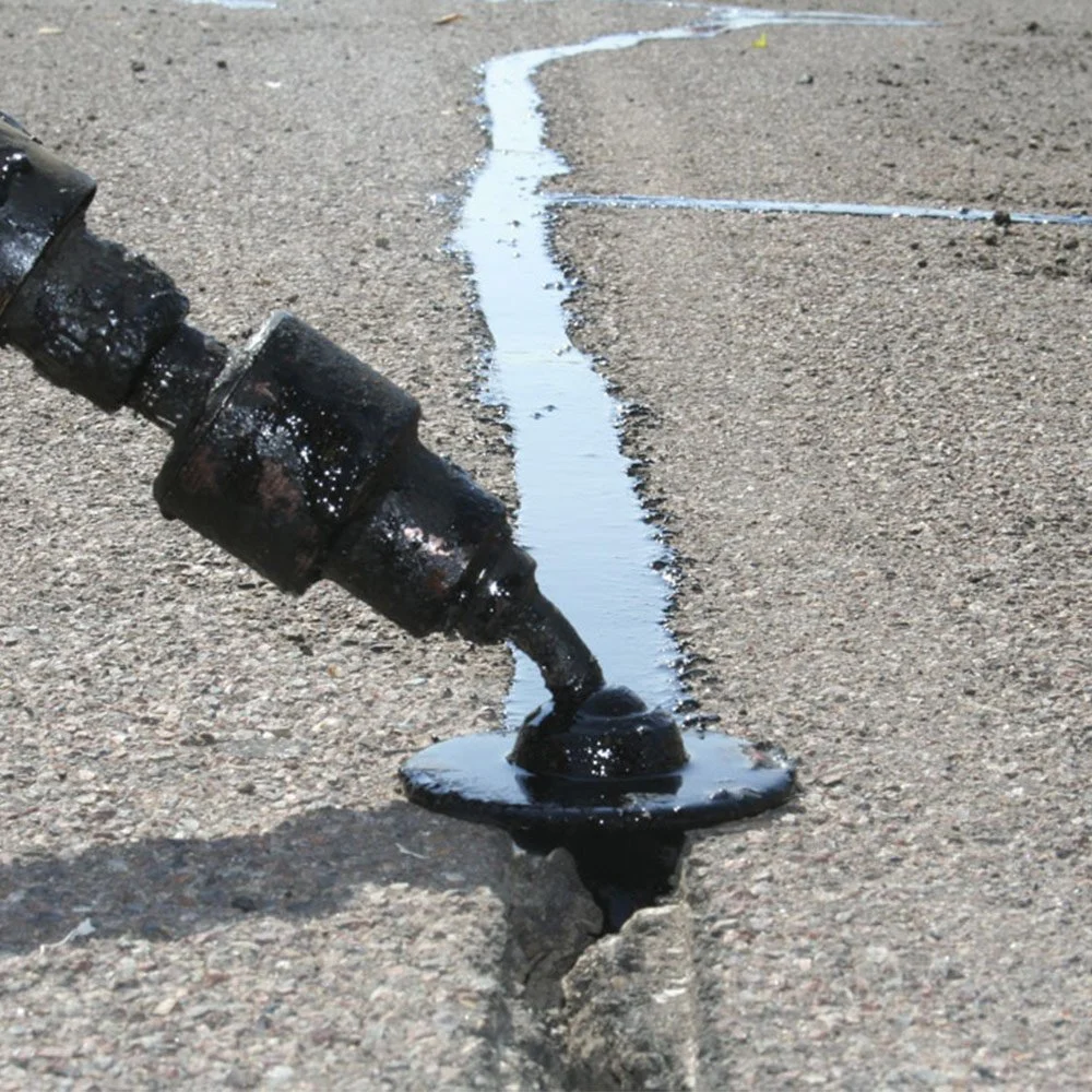 Close-up of a crack in the pavement with black liquid leaking from a broken pipe.