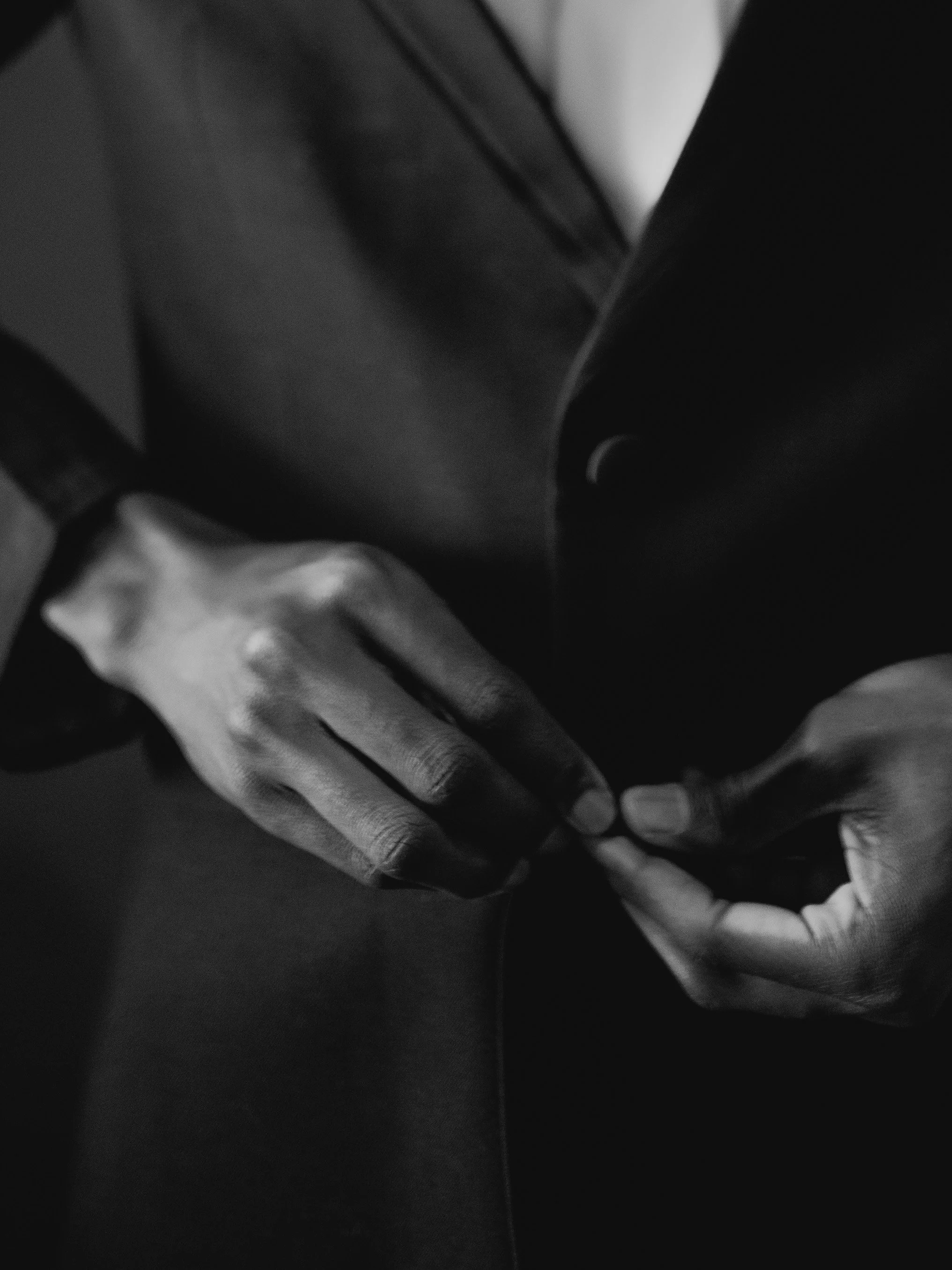 A close-up of a person's hand holding a pen, with a suit jacket sleeve visible. The image is in black and white.