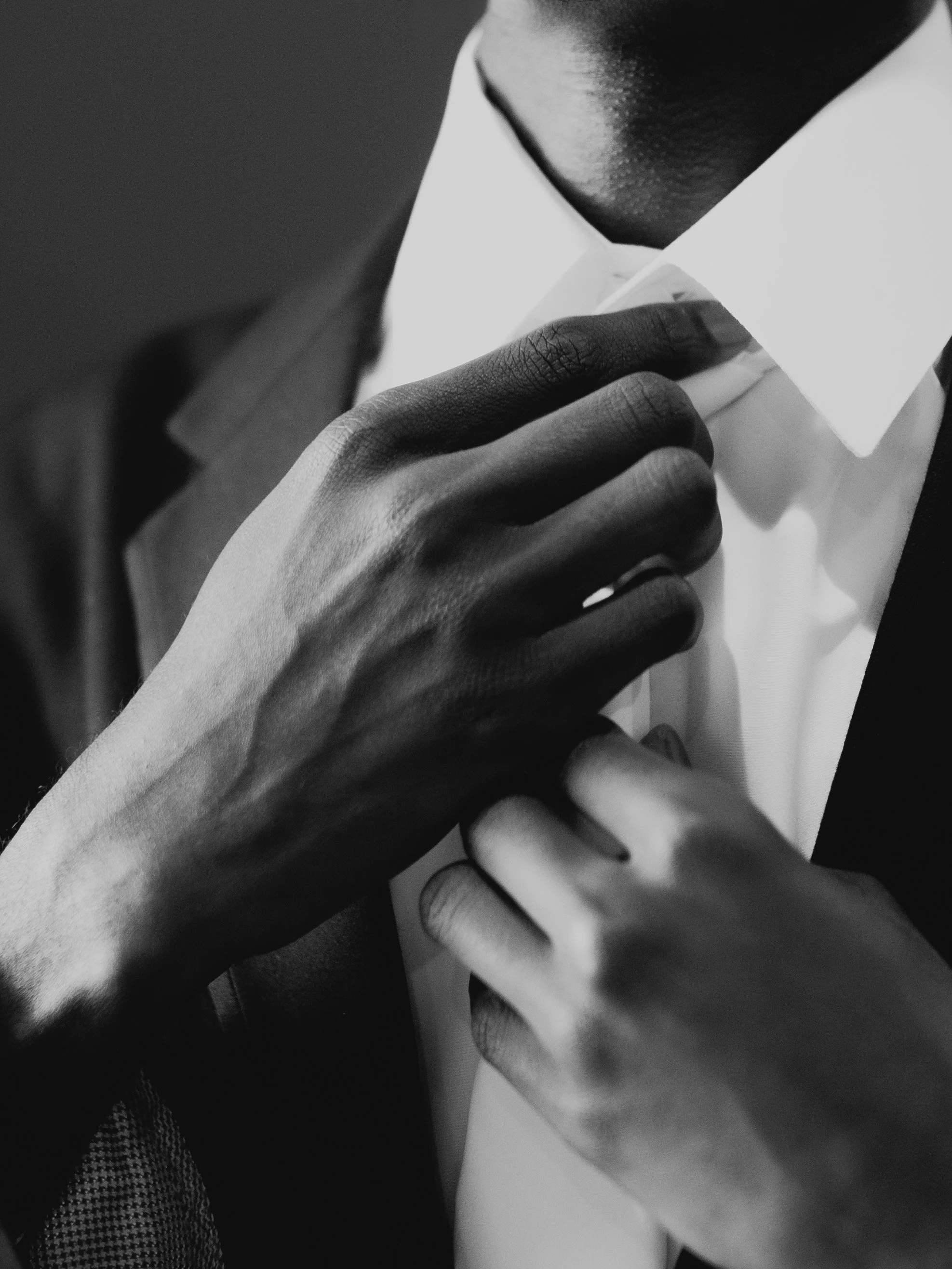 Close-up black and white photo of a person's hand adjusting a white collared shirt.