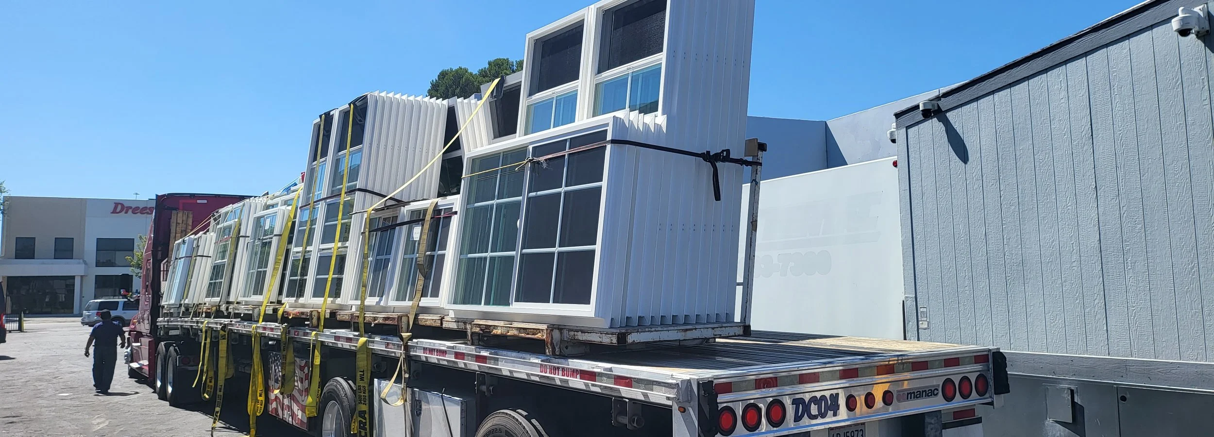 Large flatbed truck transporting multiple new glass windows and metal wall panels on a sunny day.