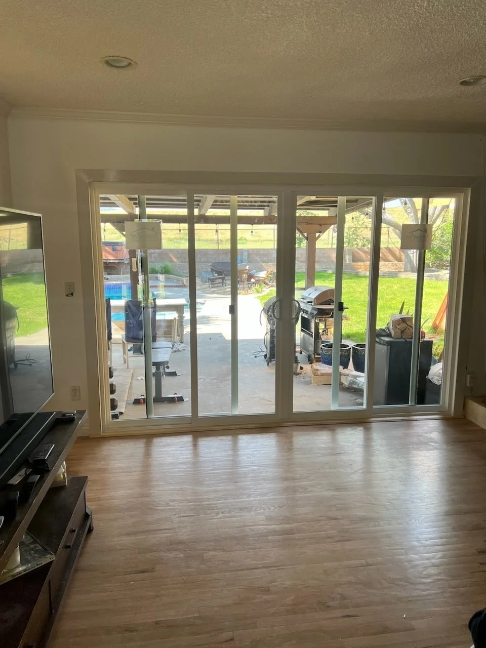 Living room with hardwood floor looking out onto a backyard with a patio, outdoor table, and chairs, through sliding glass doors.