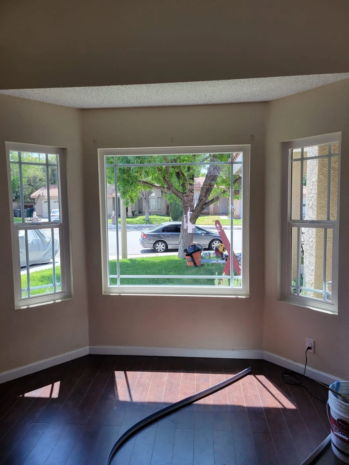 Interior view through a large front window showing a tree, street, and parked cars outside, with construction tools and materials inside.