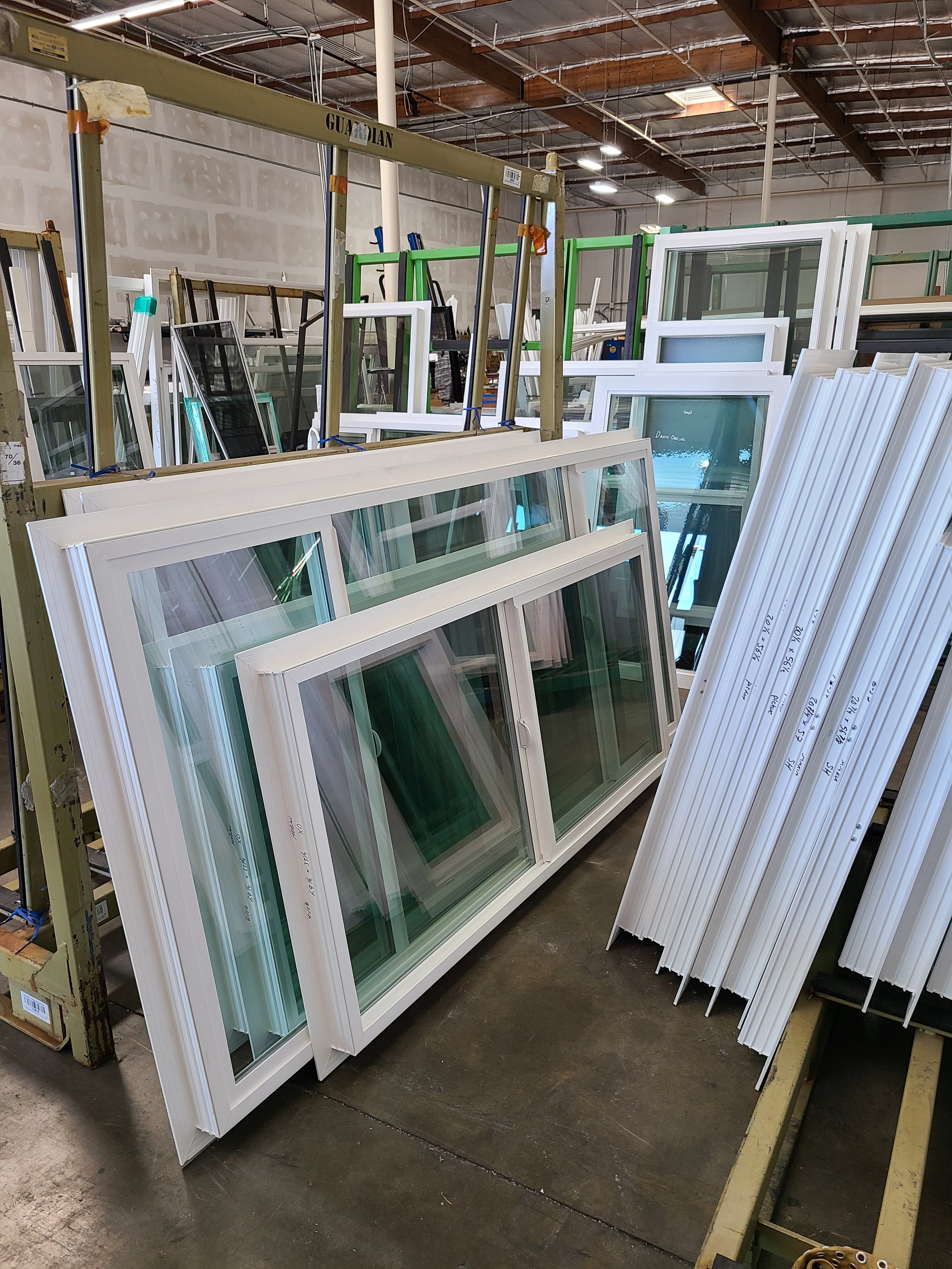 Rows of white framed windows and glass panes arranged on metal racks in a warehouse.