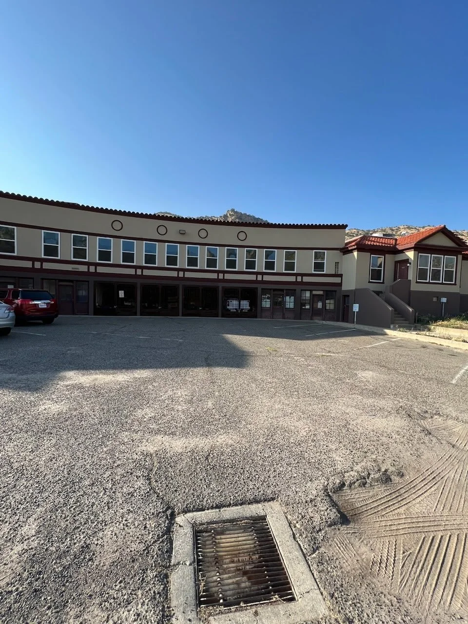 A large parking lot in front of a commercial building with multiple residential-style units, under a clear blue sky.