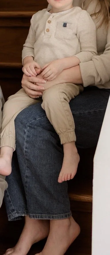 A woman and a child sitting together on stairs, with the child's legs resting on the woman's lap.