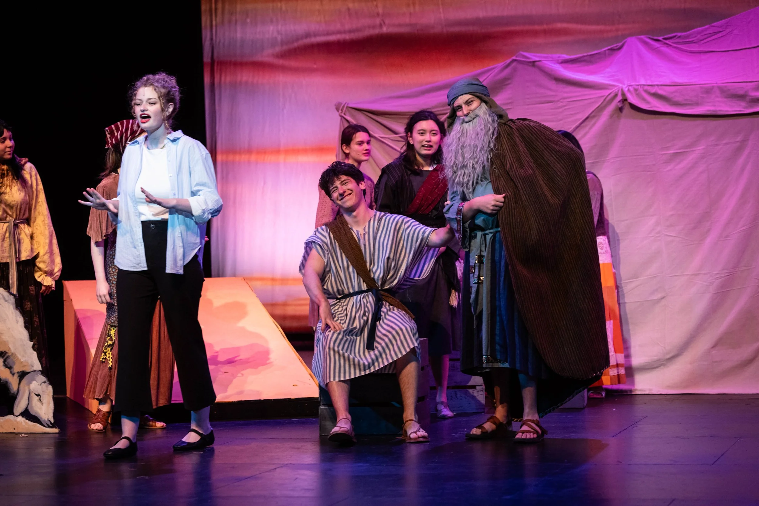 Actors on stage performing in a theatrical play with colorful costumes and set design.